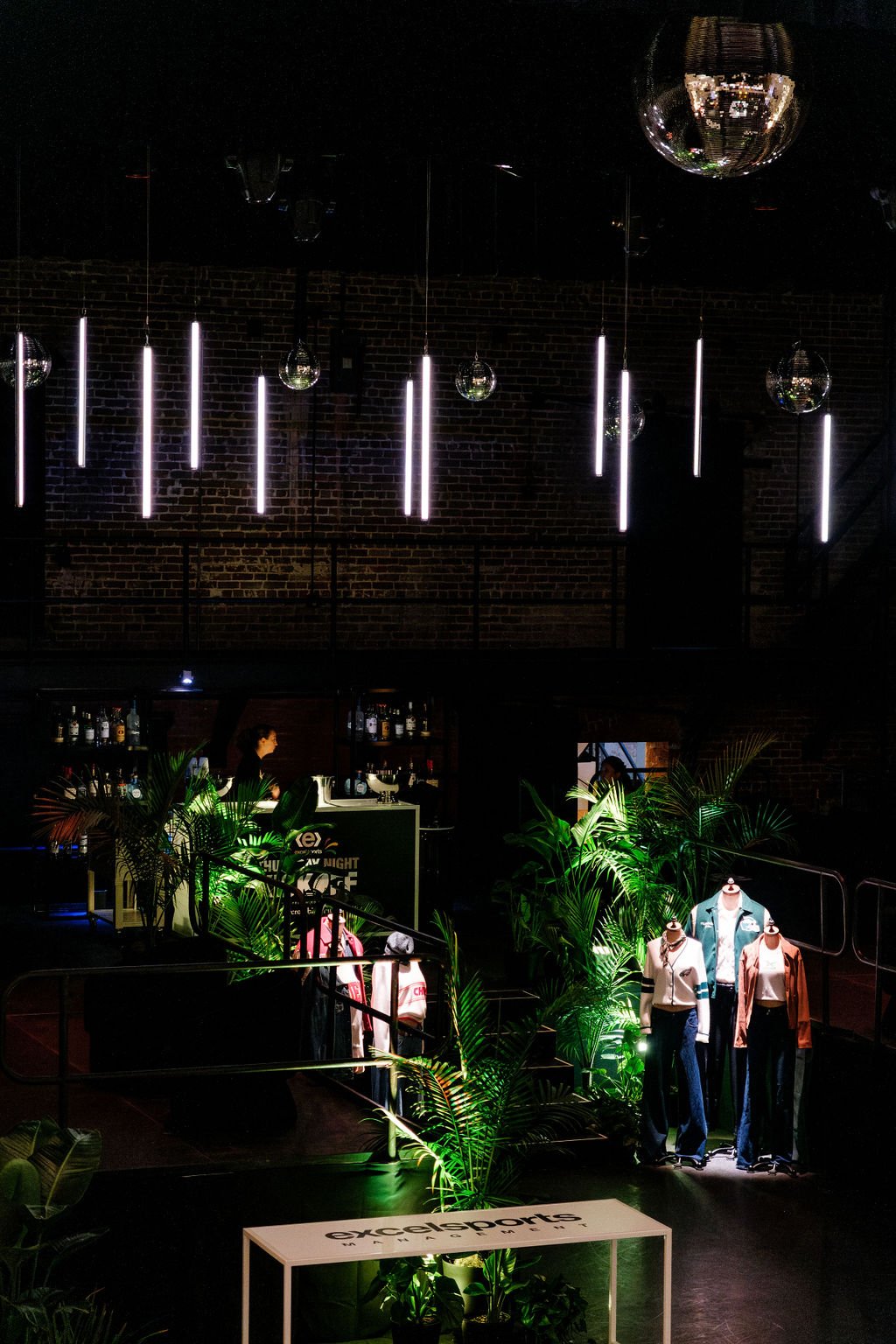 Interior of a nightclub illuminated by green lights highlighting mannequins dressed in casual clothing near lush green plants by Jungle Truck.