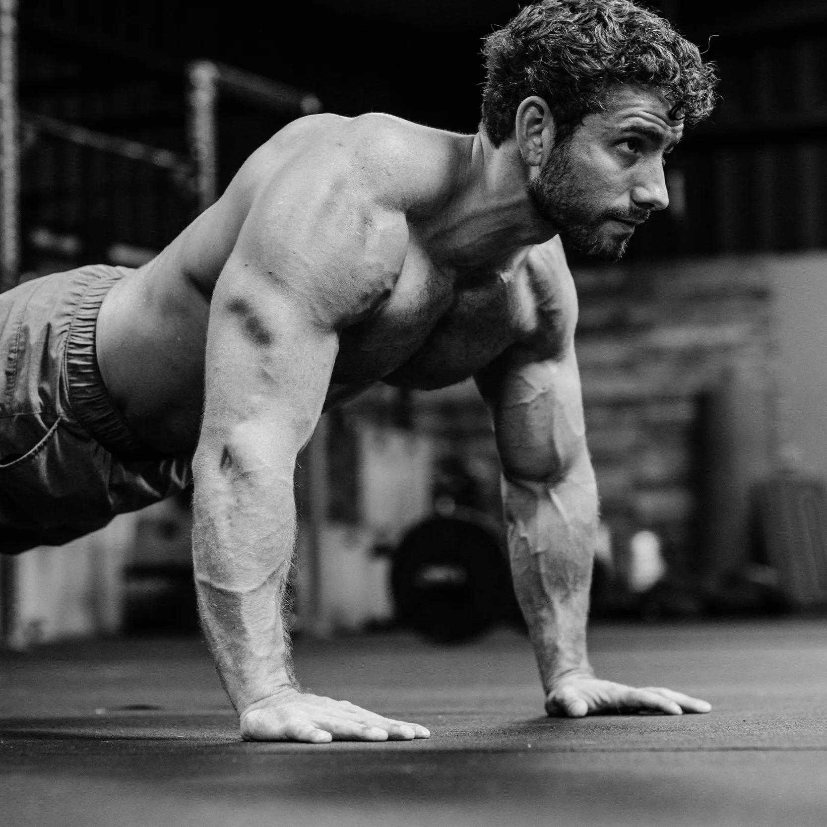 A man with curly hair and a beard doing push-ups in a gym, black and white photo.