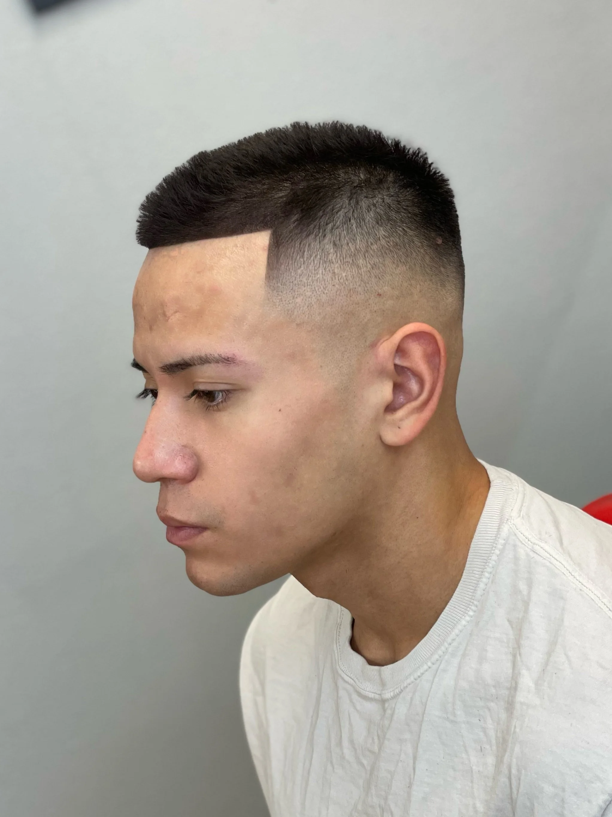 Young man with a high fade haircut, styled in a short, textured top, against a light gray background- men's haircut Las Vegas- Yoboy the Barber.
