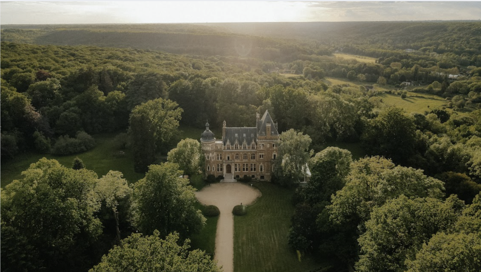 Un château victorien entouré d'une forêt dense, vue aérienne à l'approche du coucher du soleil.