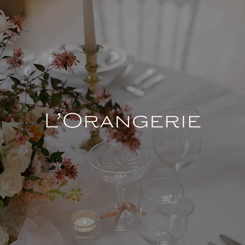 Salle de réception élégante avec tables rondes, nappes blanches, fleurs, bougies et vaisselle raffinée.