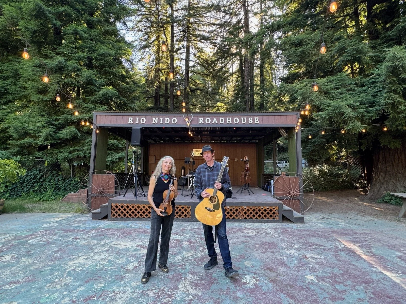 Suzuki Cady and Jimmy Murphy holding instruments in front of the Rio Nido Roadhouse stage