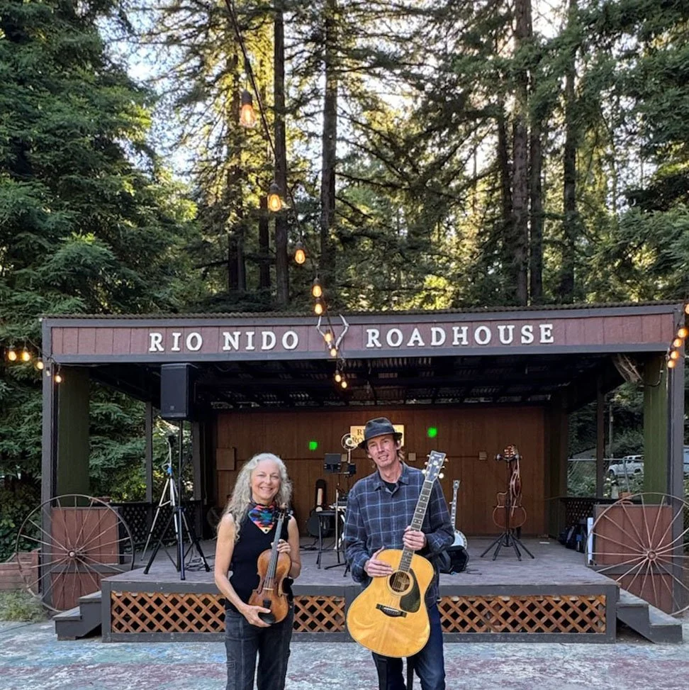 Suzuki Cady and Jimmy Murphy holding instruments in front of the Rio Nido Roadhouse stage