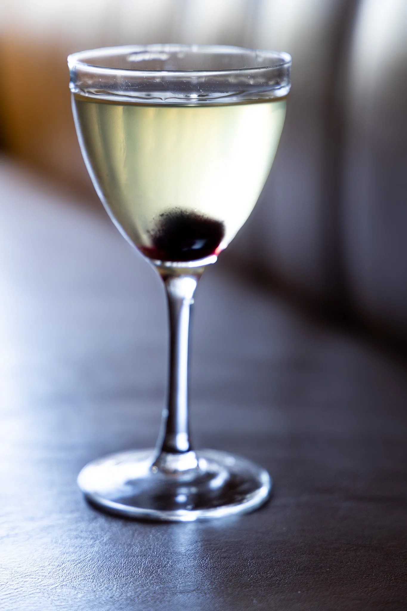 Craft cocktail, resting on a dark surface, with a blurred background.