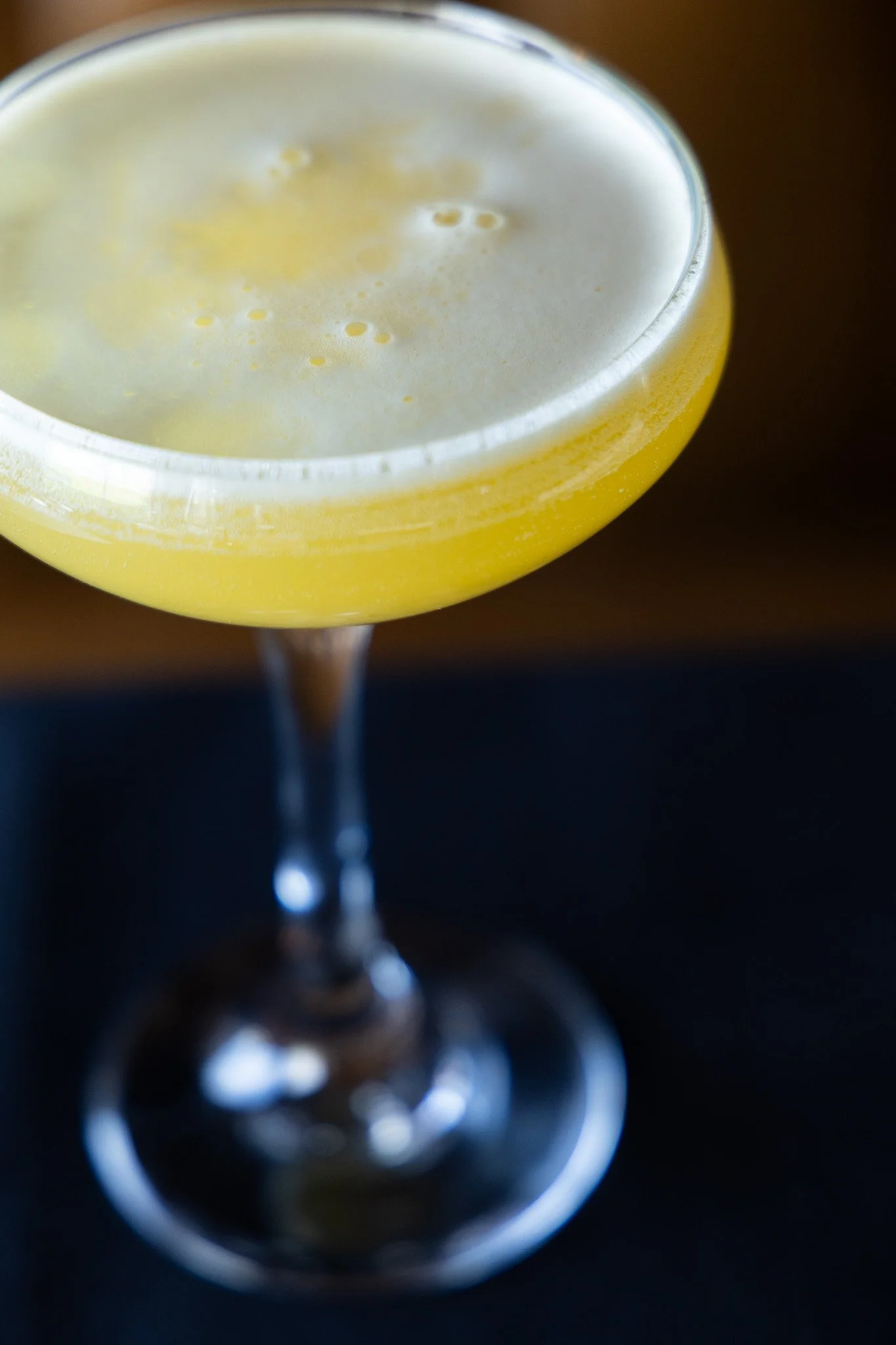A yellow cocktail in a coupe glass with a foamy top.