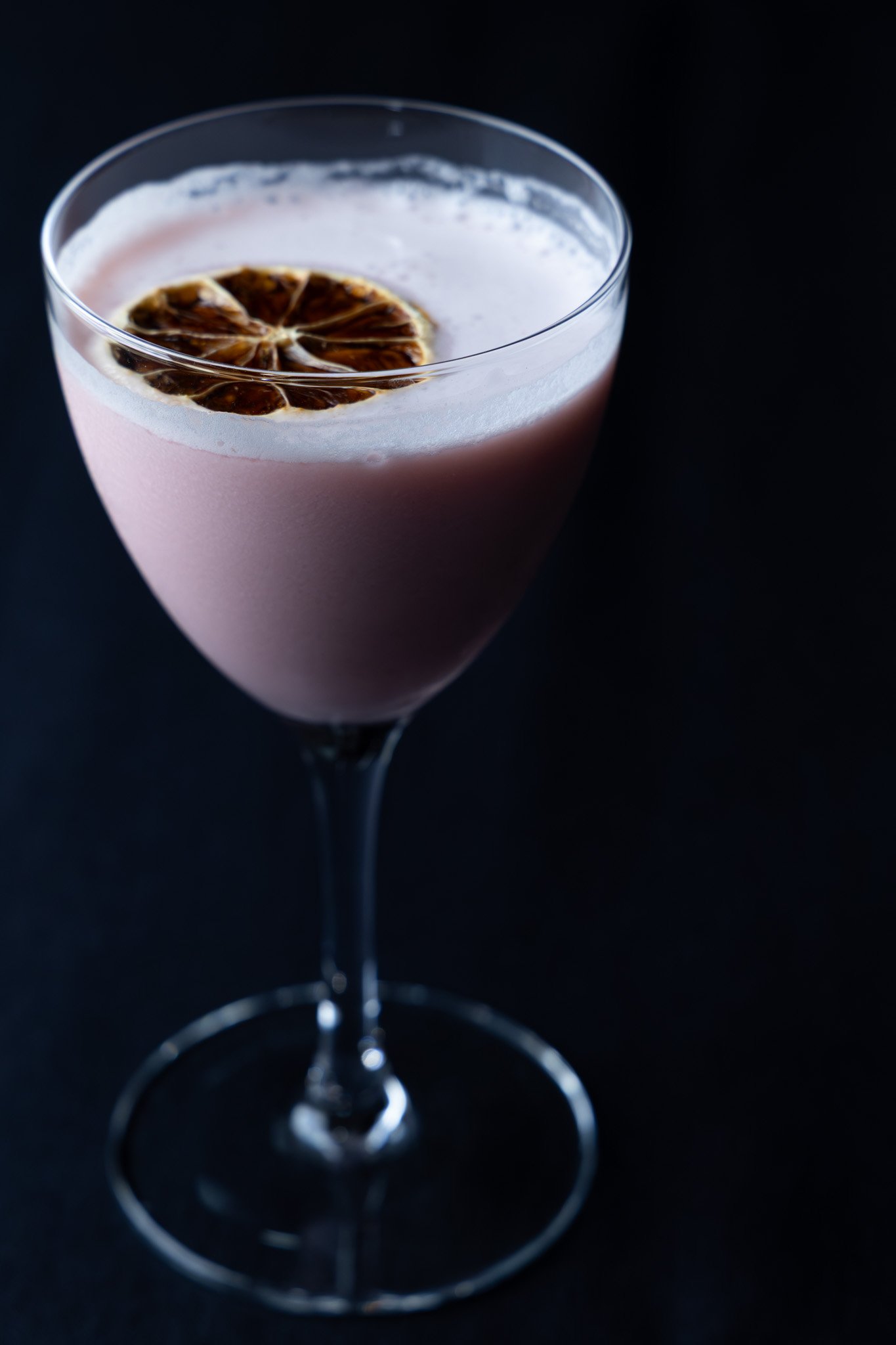 Pale pink craft cocktail with a dried citrus garnish, served in a stemmed glass at Benaiahs Scratch Kitchen.