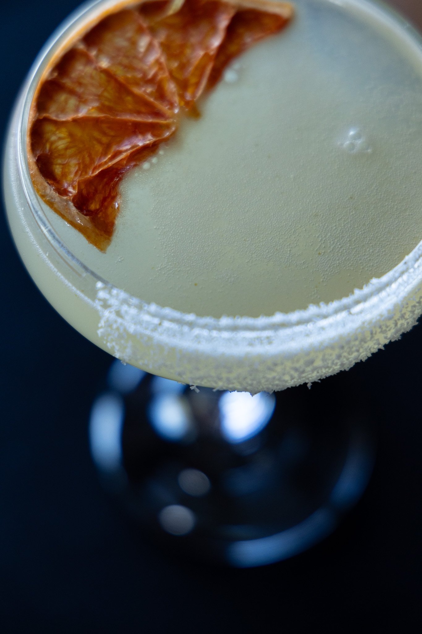Close-up of a white cocktail garnished with grapefruit, with a salted rim and a black background.