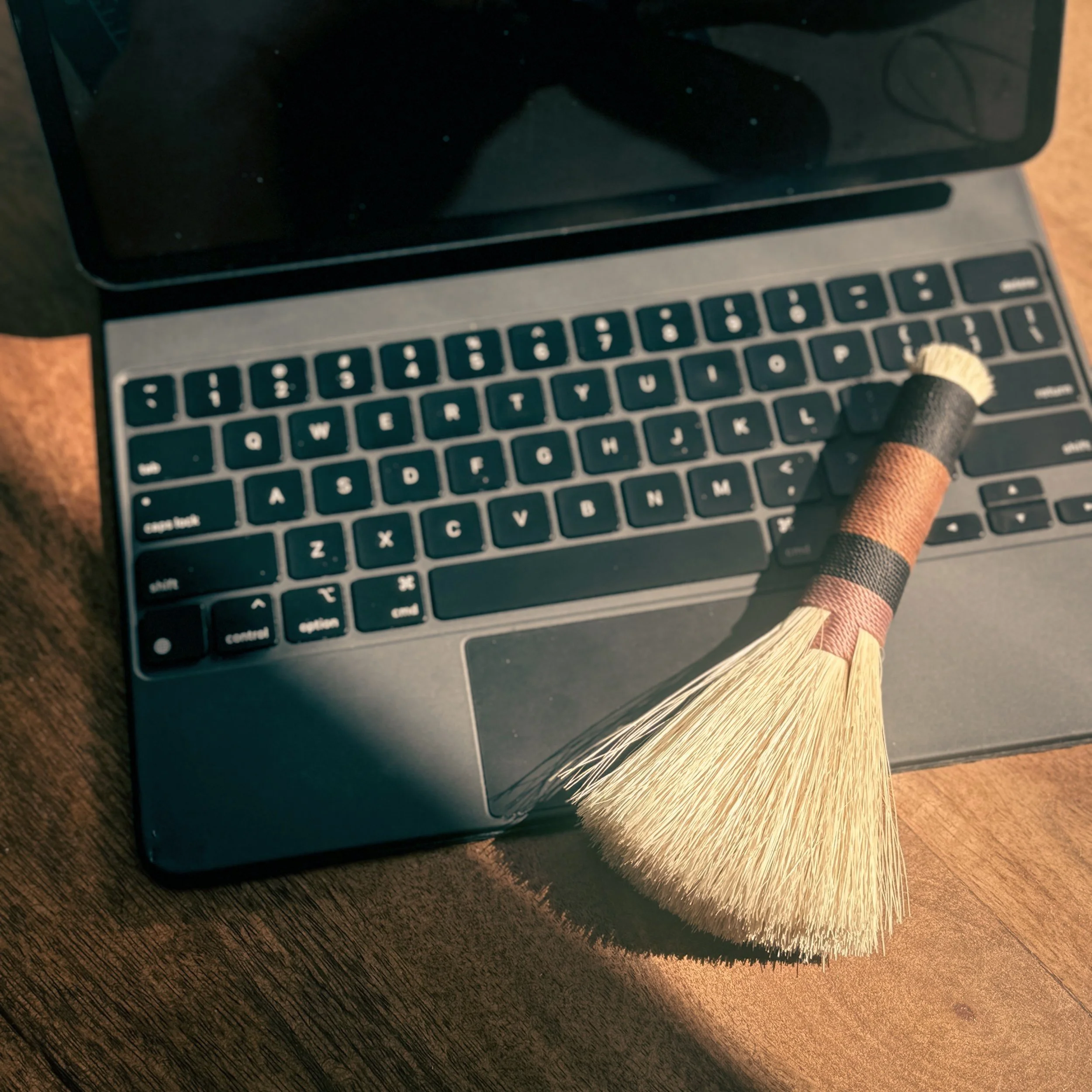 A laptop computer with a small broom resting on the keyboard.