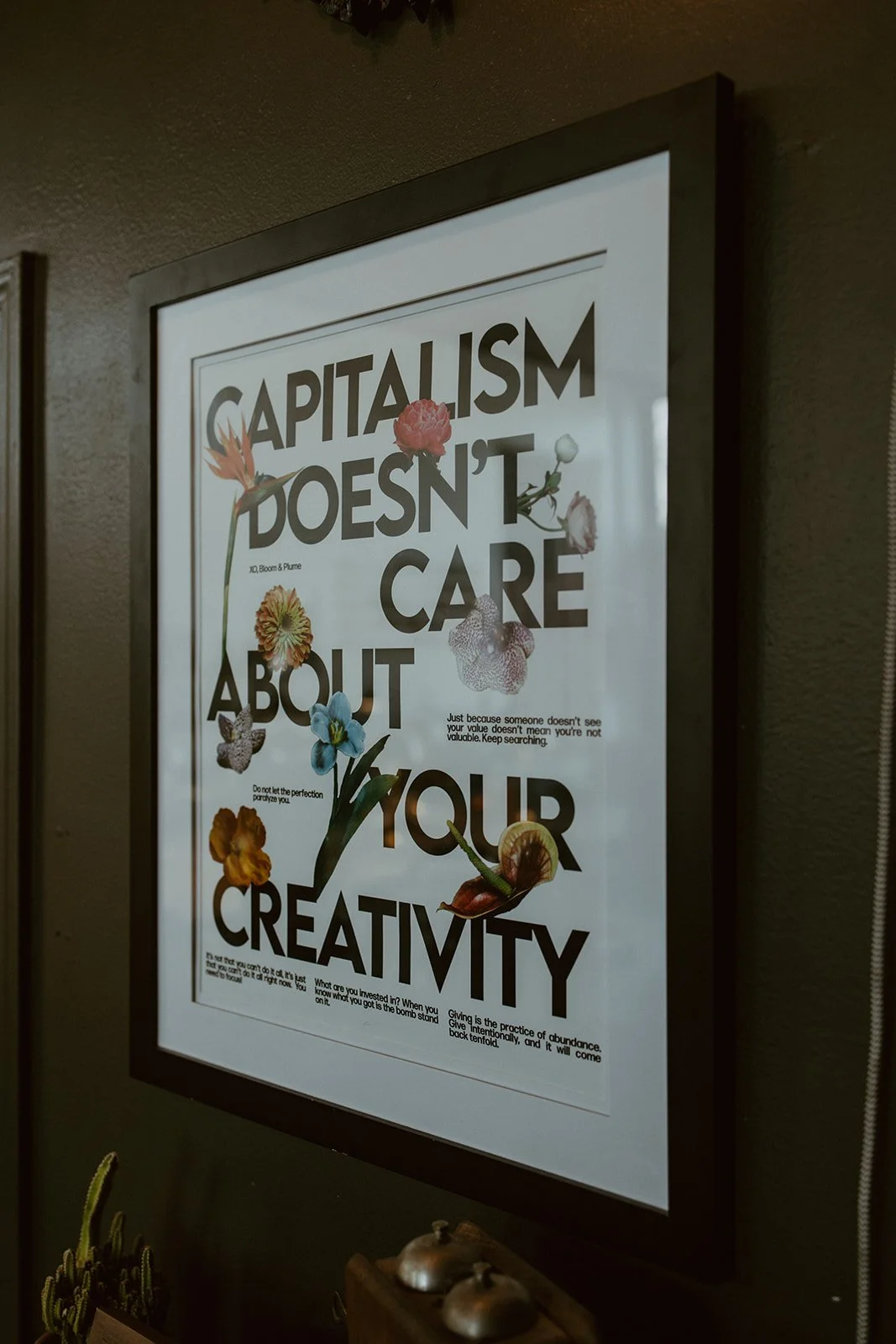 Framed poster with the quote 'Capitalism doesn't care about your creativity' decorated with colorful flowers and small text at the bottom.