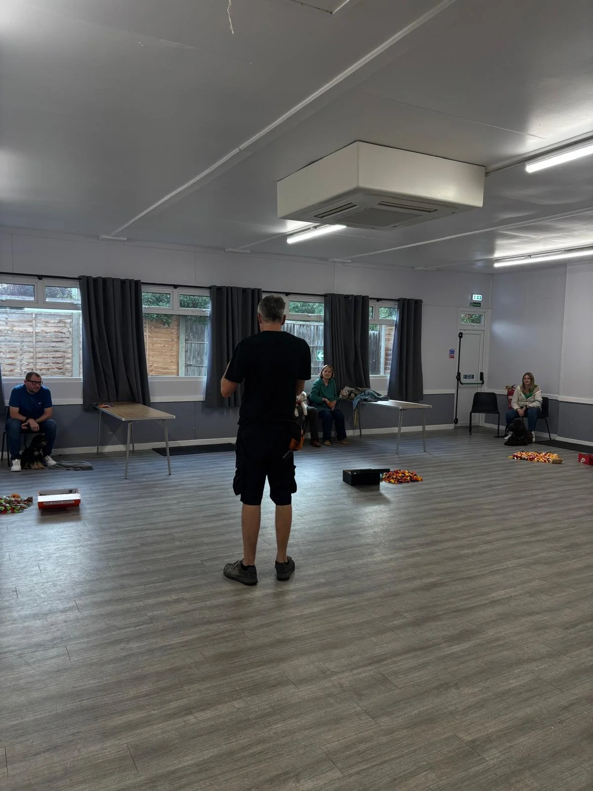 A Puppy trainer in a puppy class with several puppy owners there to train their dogs. There are enrichment items on the floor, a happy, relaxed training session