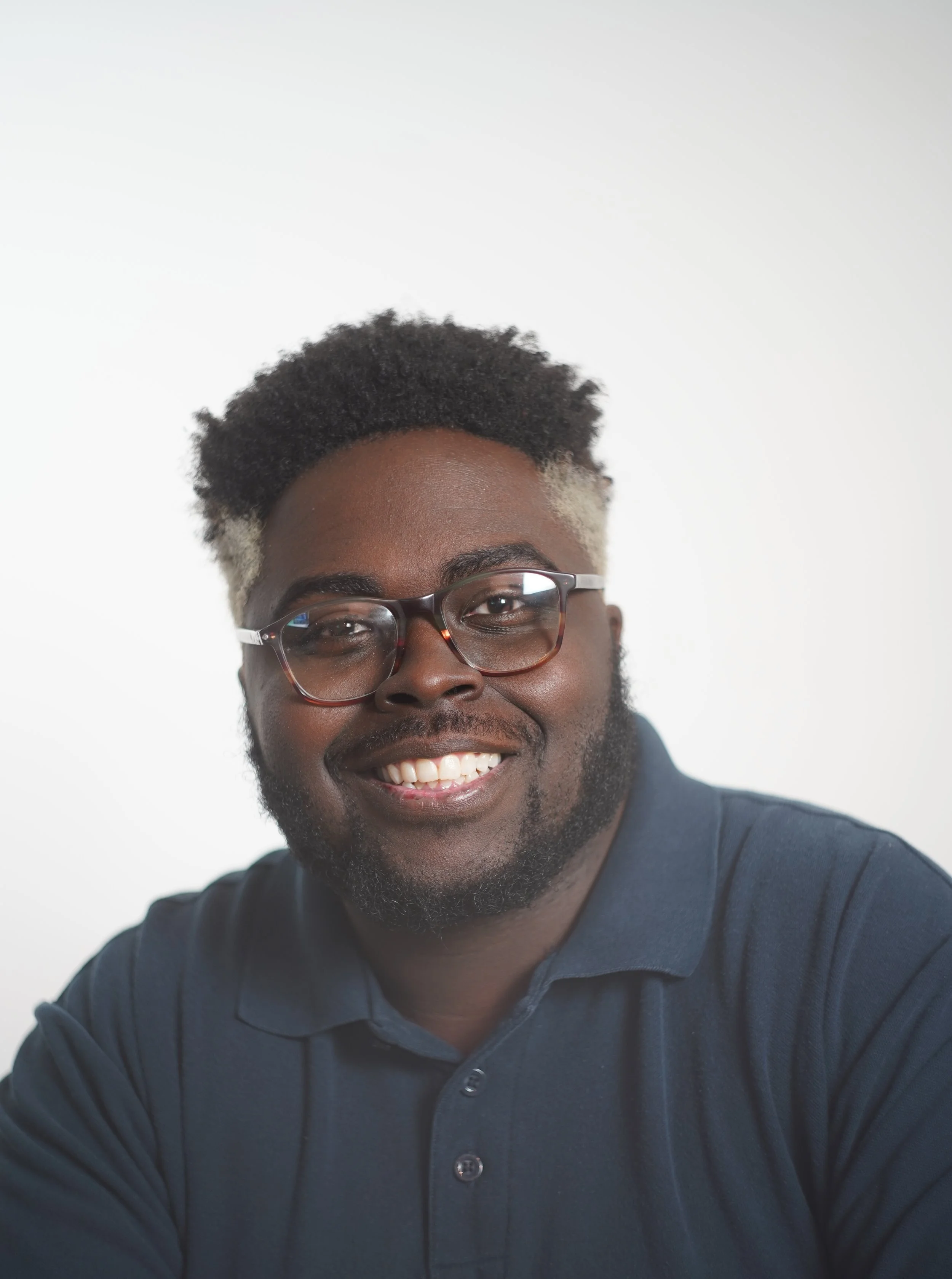 Portrait of a smiling man wearing glasses and a dark polo shirt, against a plain white background.