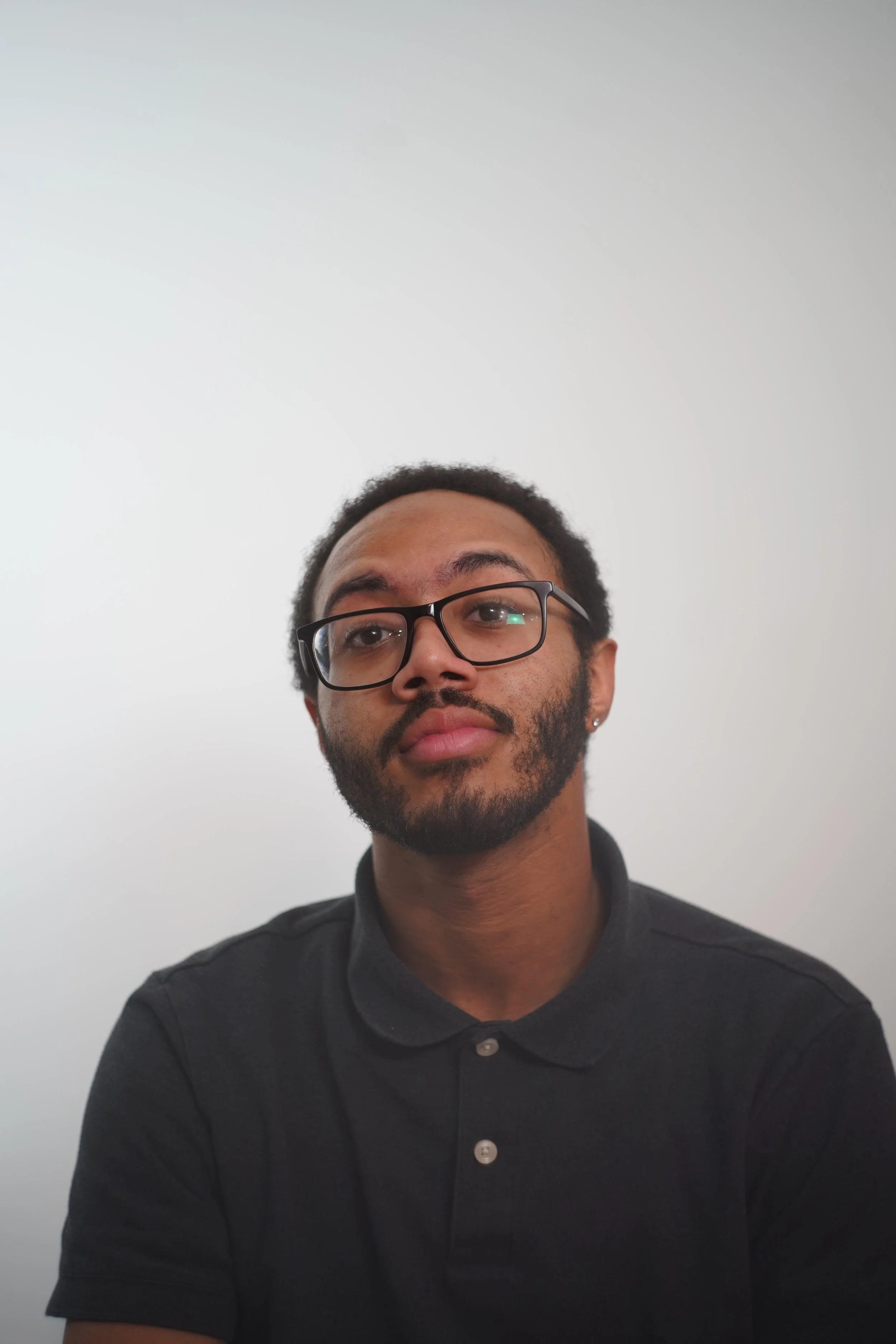 Portrait of a young man wearing glasses and a black polo shirt against a plain white background.