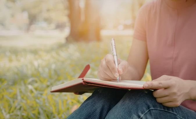 A person sitting in a relaxing forest beginning their fertility journey taking notes in a journal