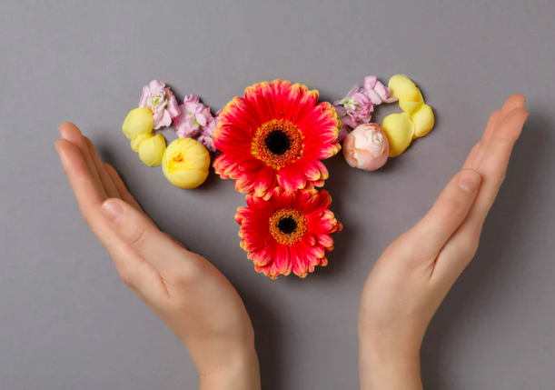 Image of hands embracing a representation of a uterus and ovaries made of flowers to symbolize having a grasp on one's menstrual rhythms.