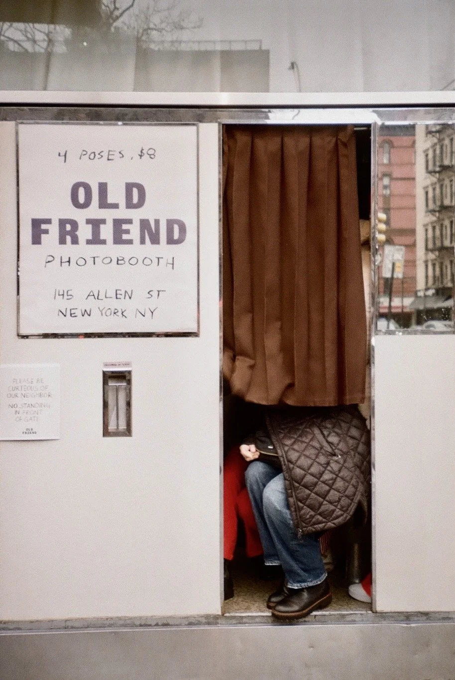 Photobooth with a person sitting inside, partially visible, at Old Friend Photobooth on Allen Street, New York.