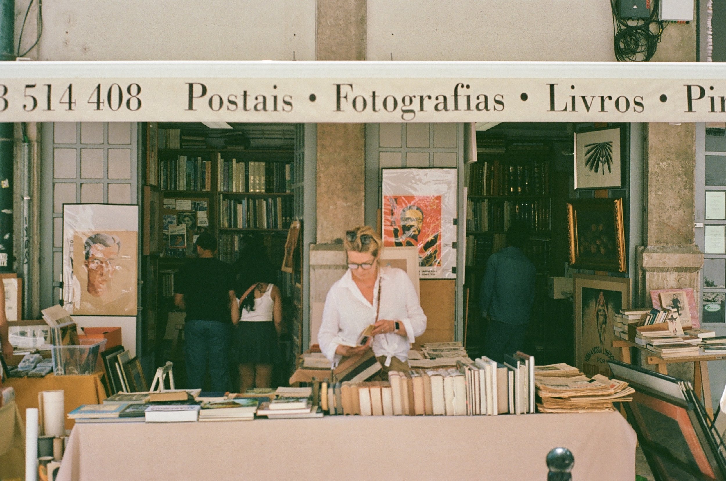 Outdoor bookshop with books, paintings, and photographs for sale. People browsing.