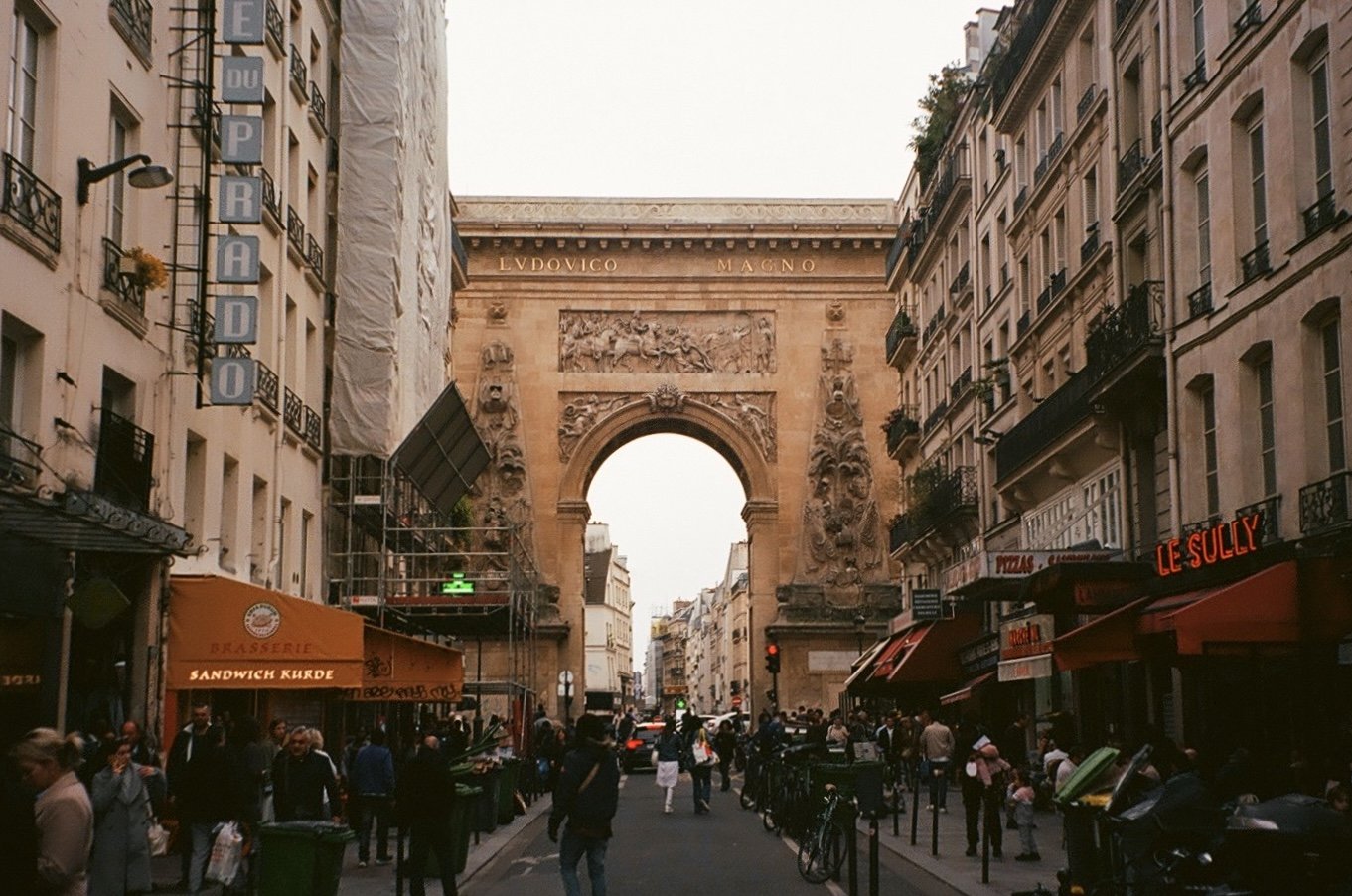Street view of Porte Saint-Denis in Paris with shops and people walking.