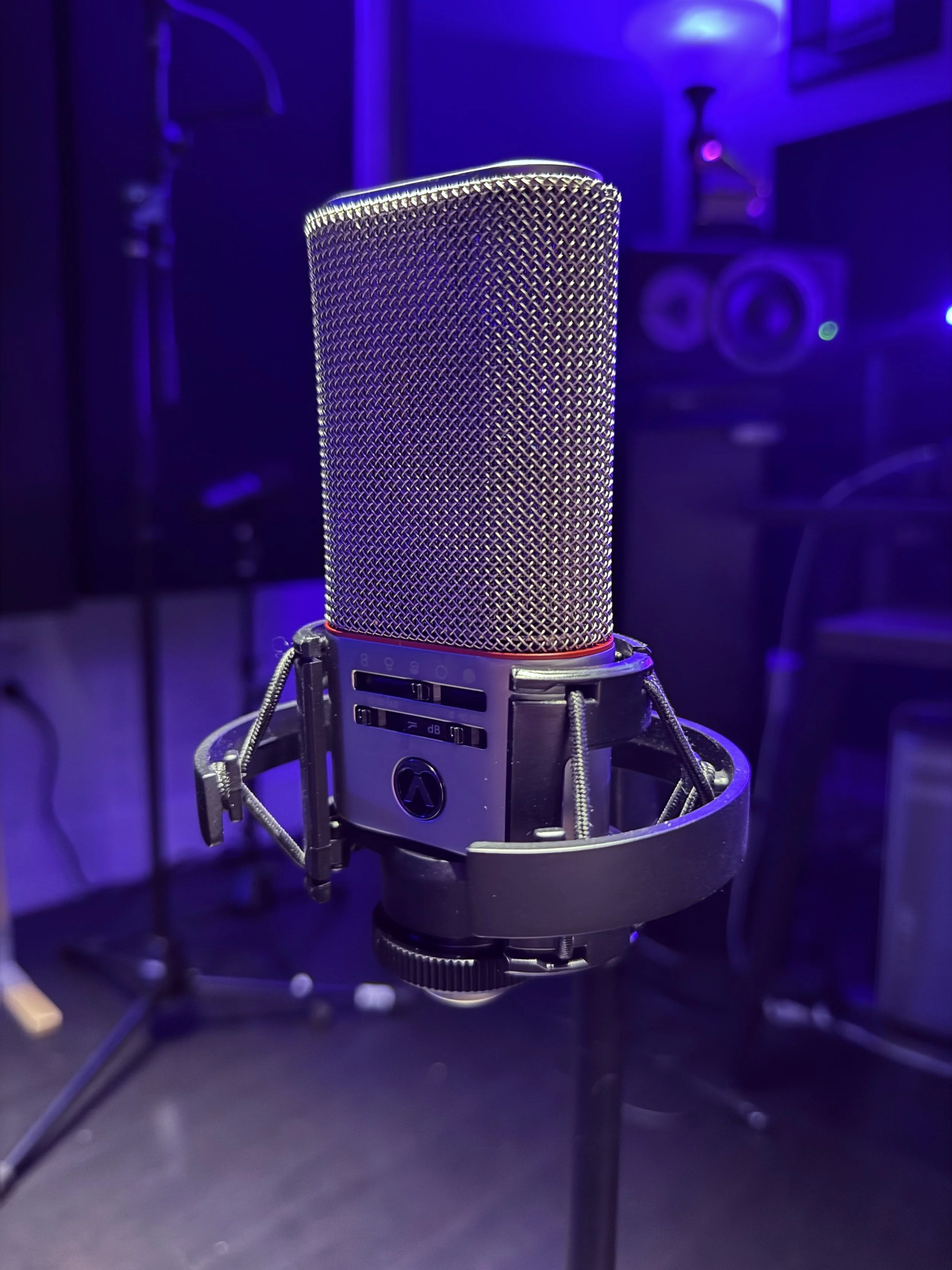 A professional studio microphone, The 818 by Austrian Audio, mounted on a shock mount in a recording studio with purple lighting.
