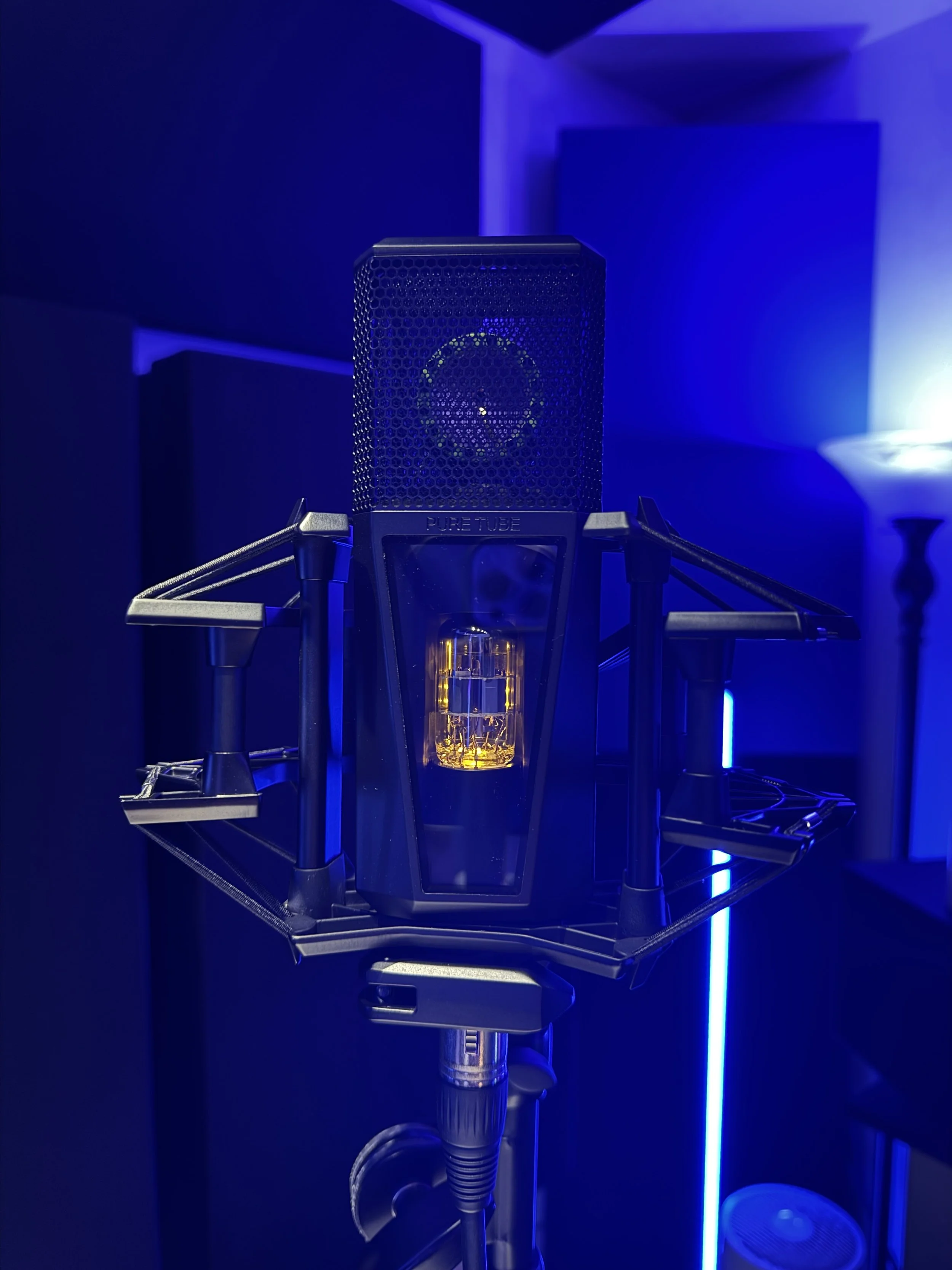 Close-up of the PURE tube microphone by Lewitt with a glowing filament visible inside, set against a dark background with blue lighting.