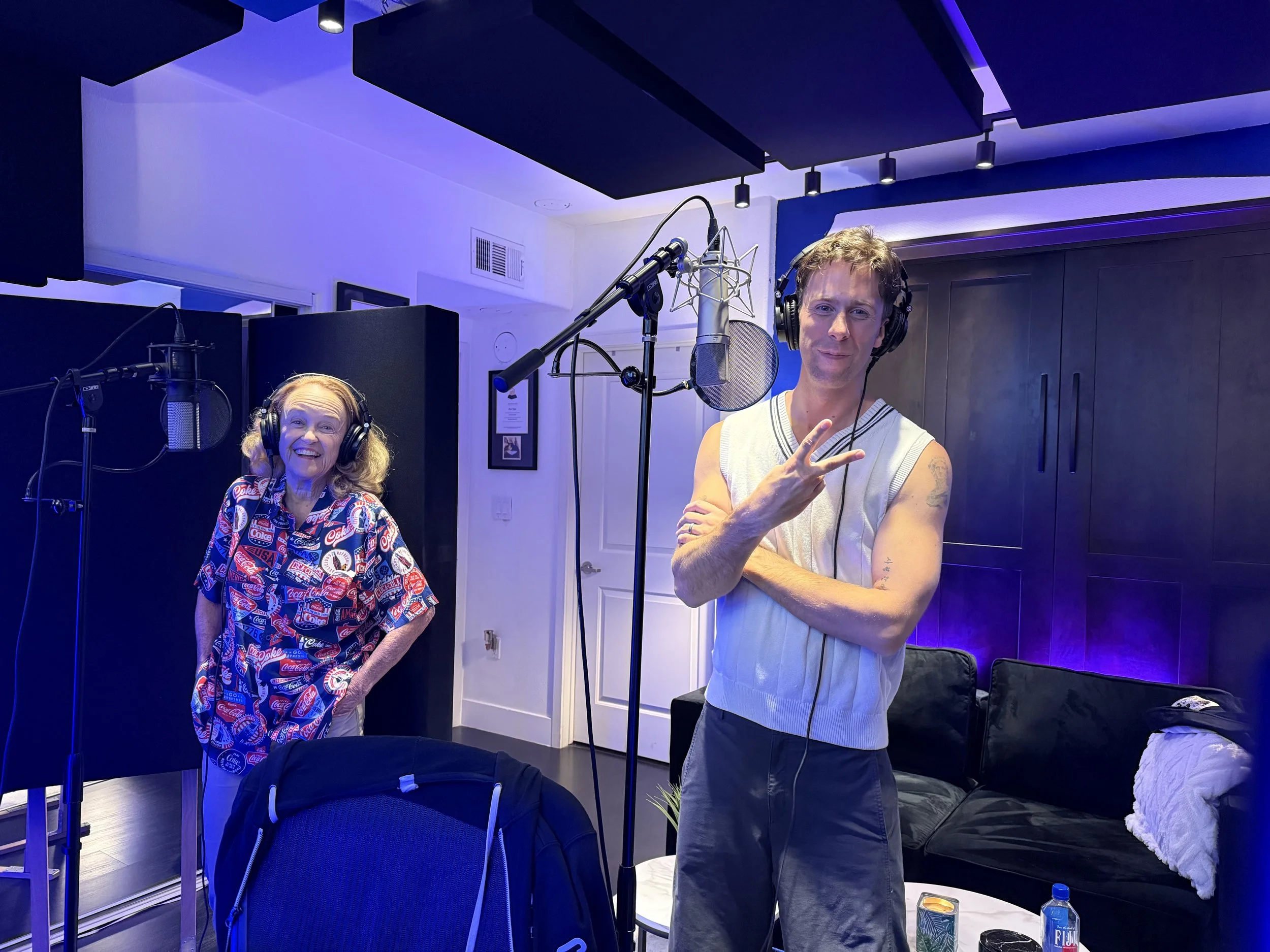 Danielle Kennedy and Briggon Snow recording audio in a professional studio. Briggon is making a peace sign to the camera.