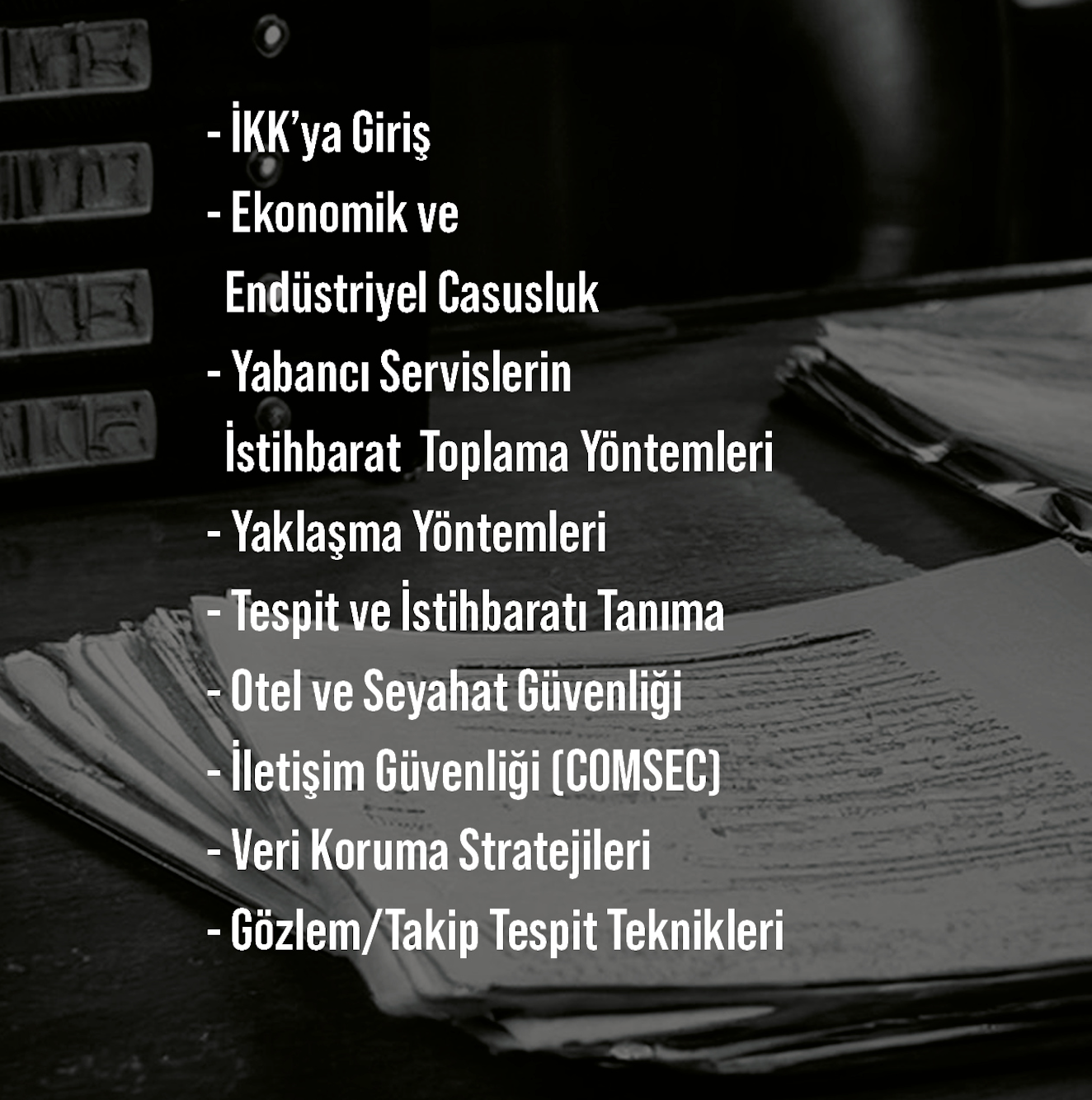 Bir masa üzerinde düzenlenmiş çeşitli belgeler ve klasörler, arka planda bilgisayarın kasası ve kitaplar bulunmaktadır. Üzerinde turuncu ve siyah renklerde yazılmışkı bazı belge ve klasörler vardır.