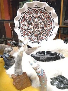 Decorative ceramic plate with intricate orange and black pattern on a table with animal figurines and a small tree sculpture.