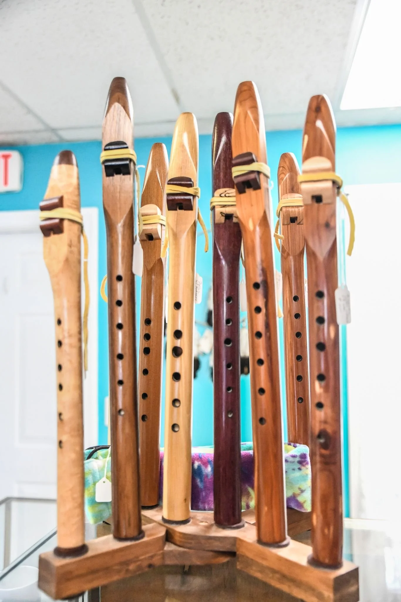 Collection of wooden flutes displayed upright on a stand in a room with blue walls.