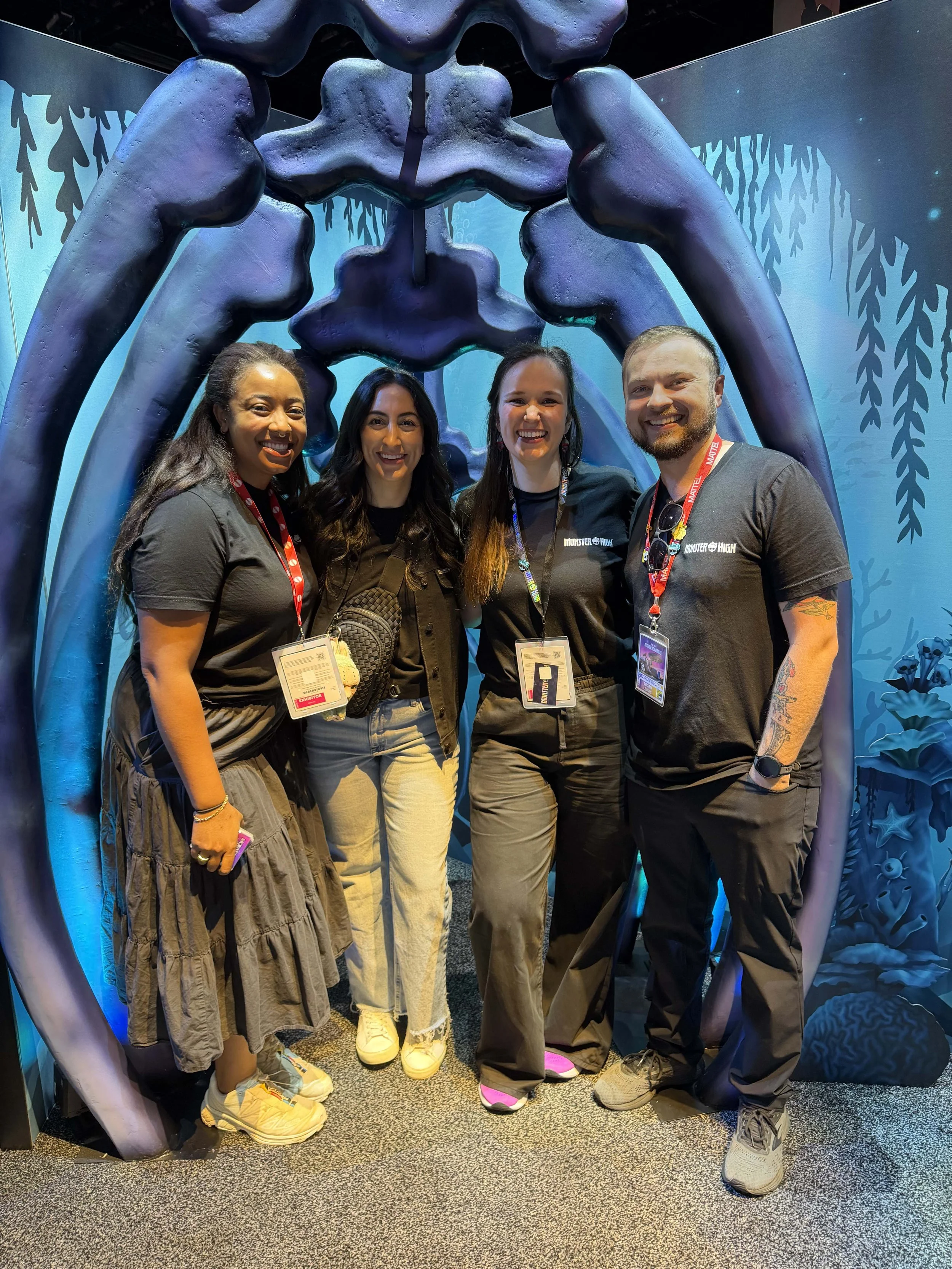 Four people smiling and standing inside a large, inflatable structure with a blue and purple design. They are at an event or convention, wearing casual clothes with event badges around their necks.