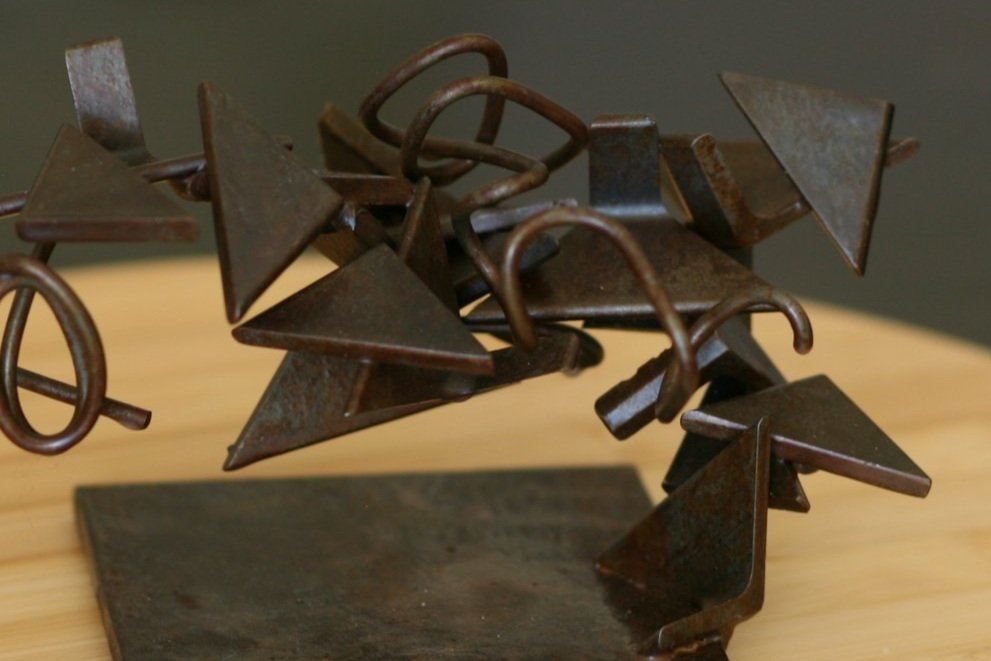Detail of Rusted steel abstract sculpture, triangular pieces and twisted rod with a base