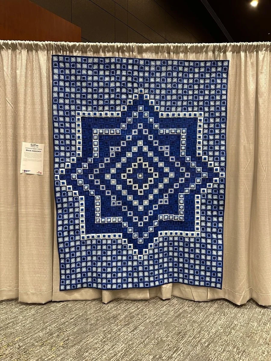 Blue quilt with geometric star pattern displayed on a beige curtain backdrop
