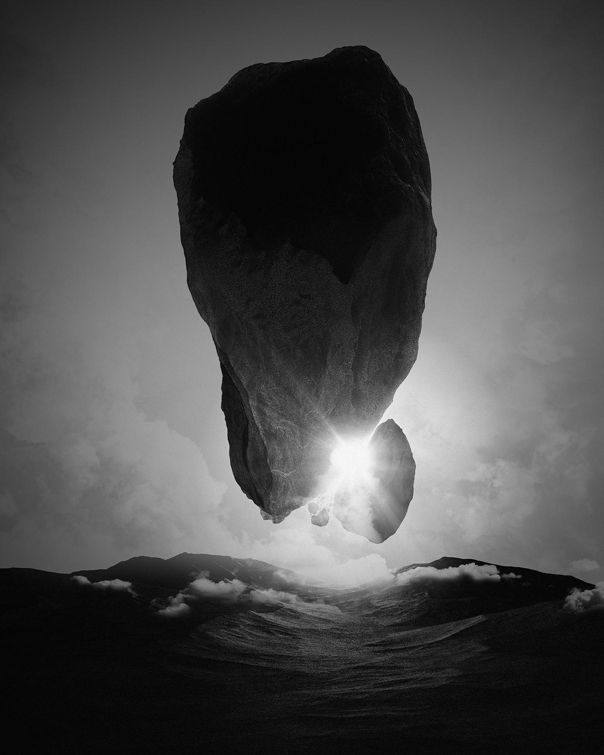 A black and white photo of a large floating rock formation above a mountainous landscape with the sun shining behind it.
