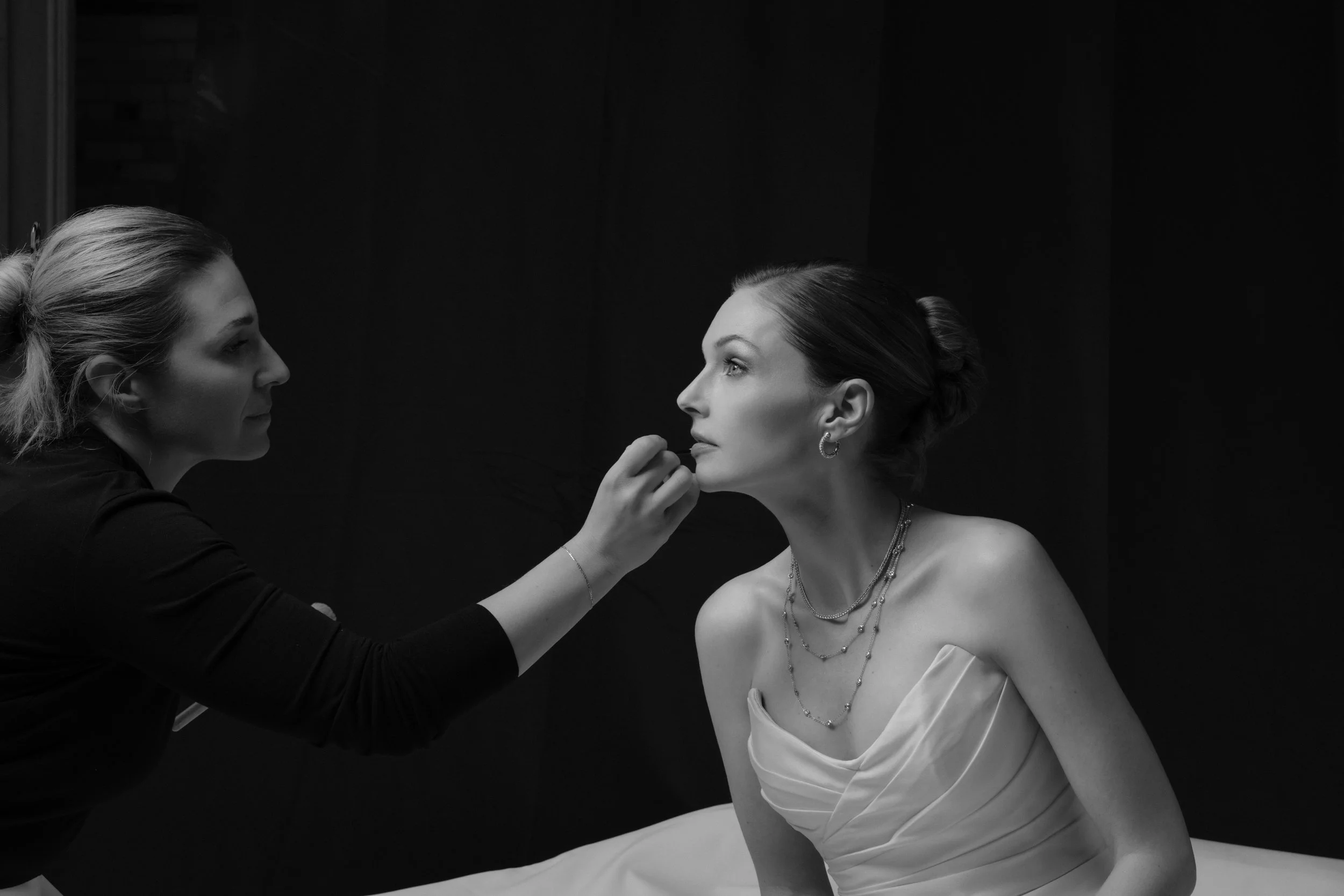A woman getting makeup applied by a makeup artist in a black-and-white photo.