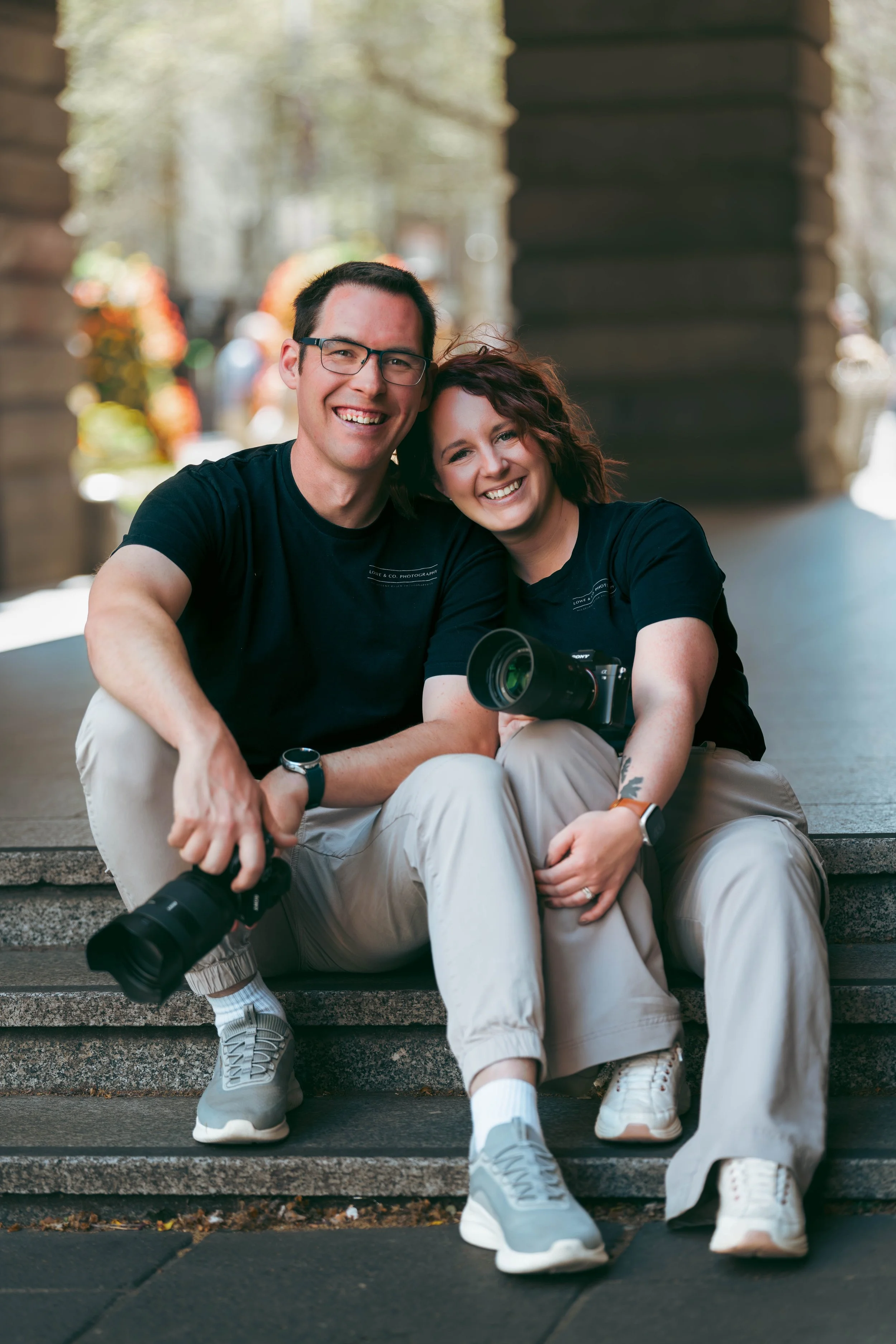 Couple holding cameras sitting cuddling on a step in the Melbourne City