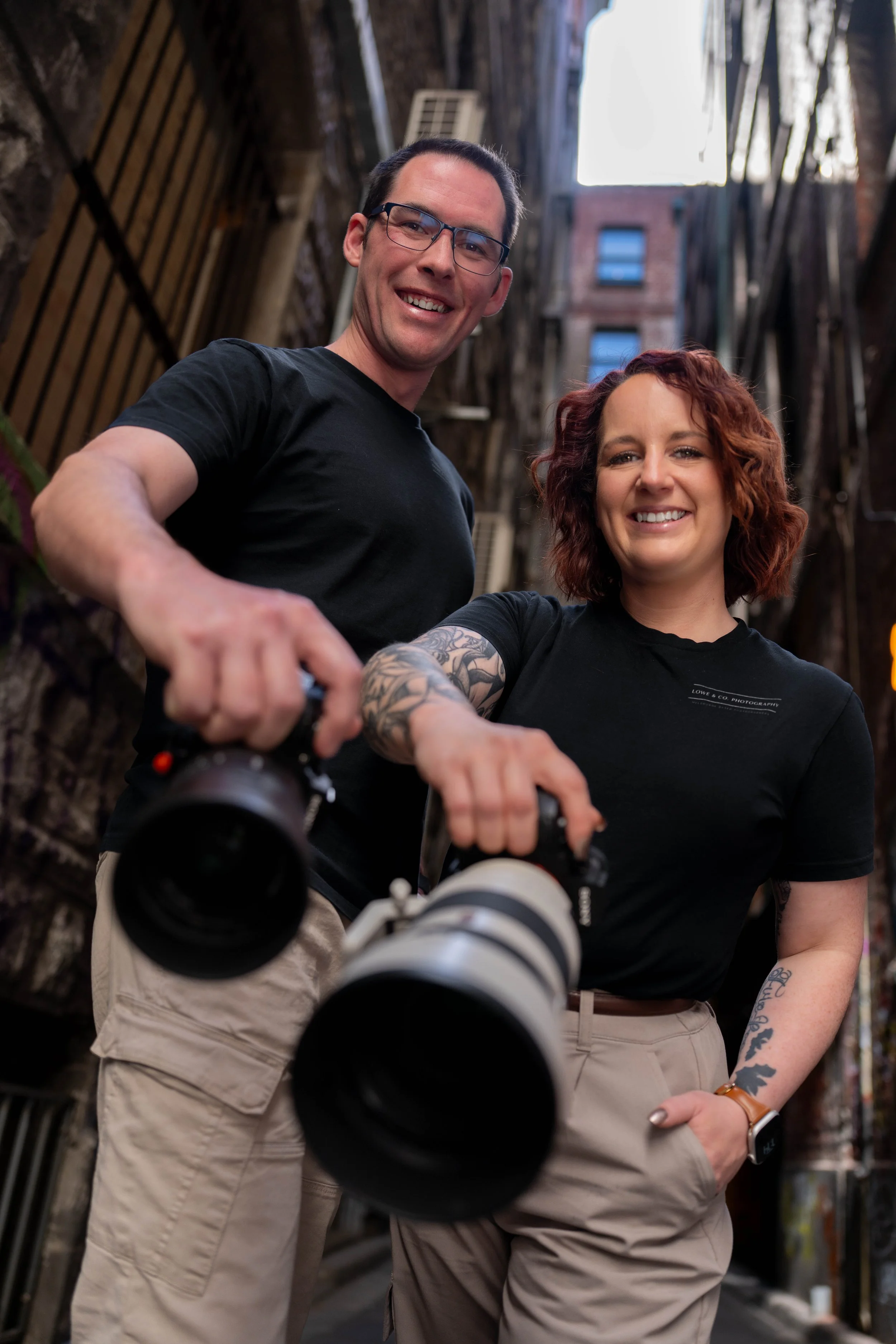 Samie & Chris two family and wedding photographers from Melbourne posing with their cameras in a lane way