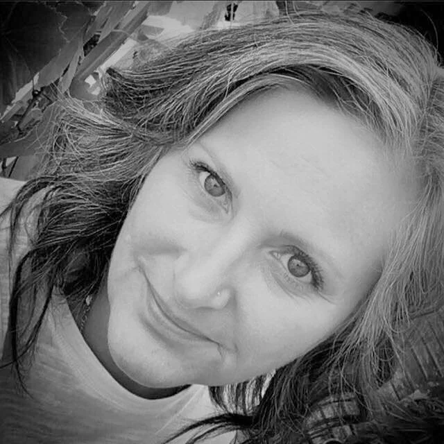 Close-up black and white photo of a woman with wavy hair, smiling and looking into the camera.