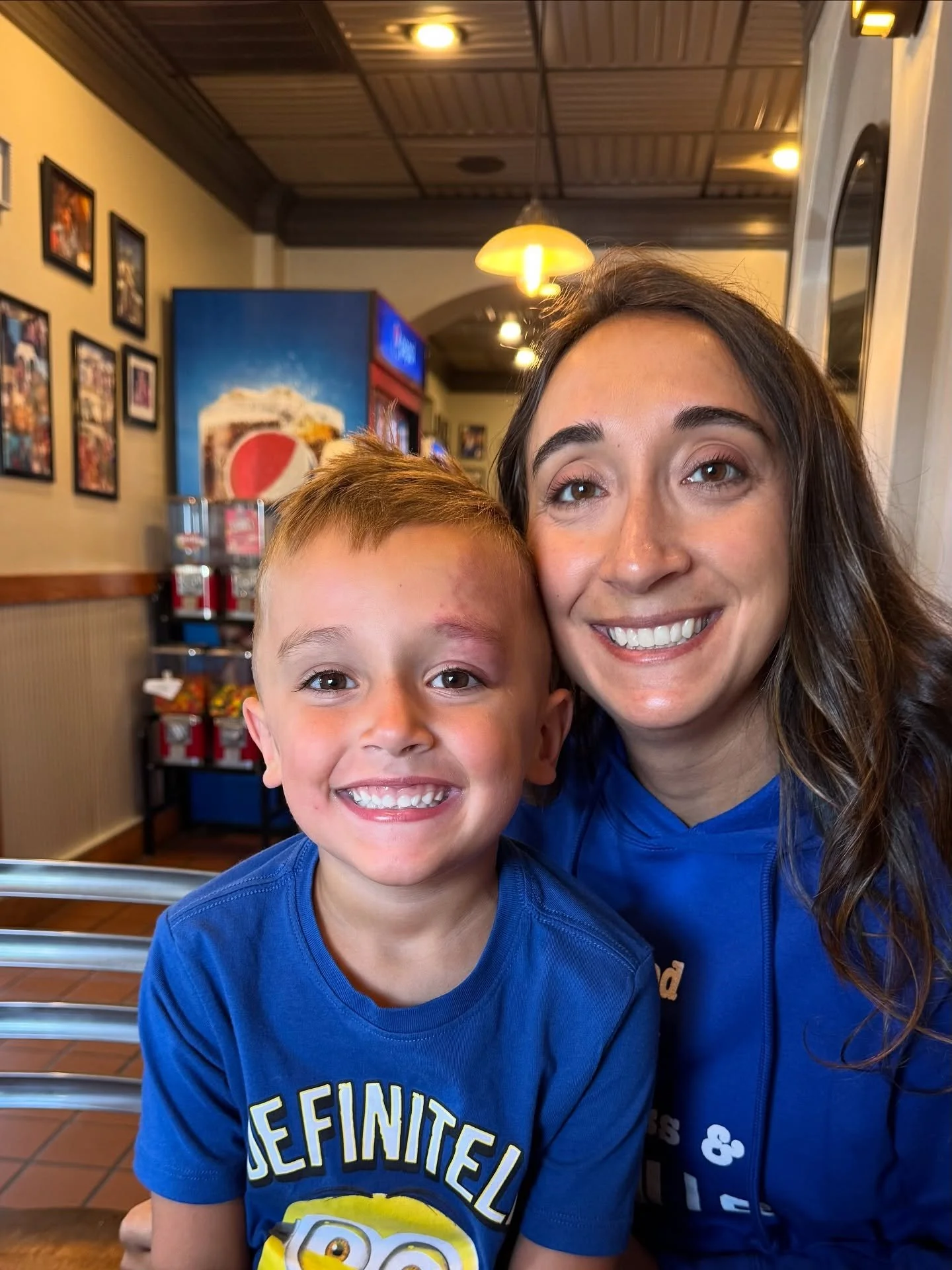 A smiling woman and a young boy taking a selfie inside a restaurant, with wall art and a drink fountain in the background.