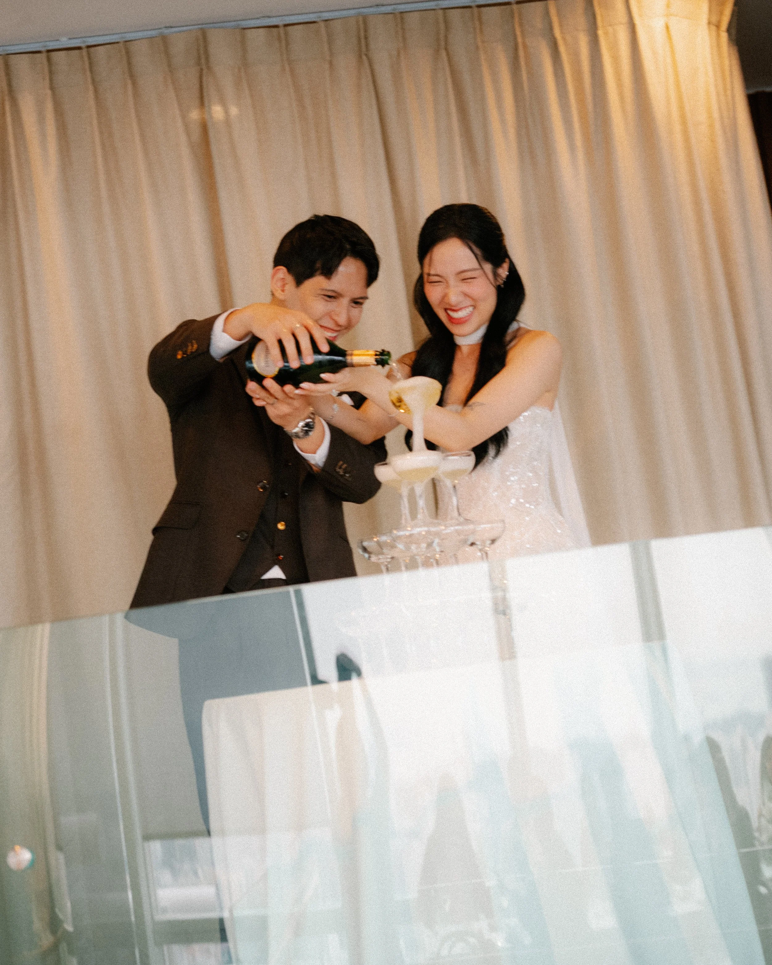 Bride and groom pouring champagne tower at modern indoor wedding reception at 1-Atico Singapore.