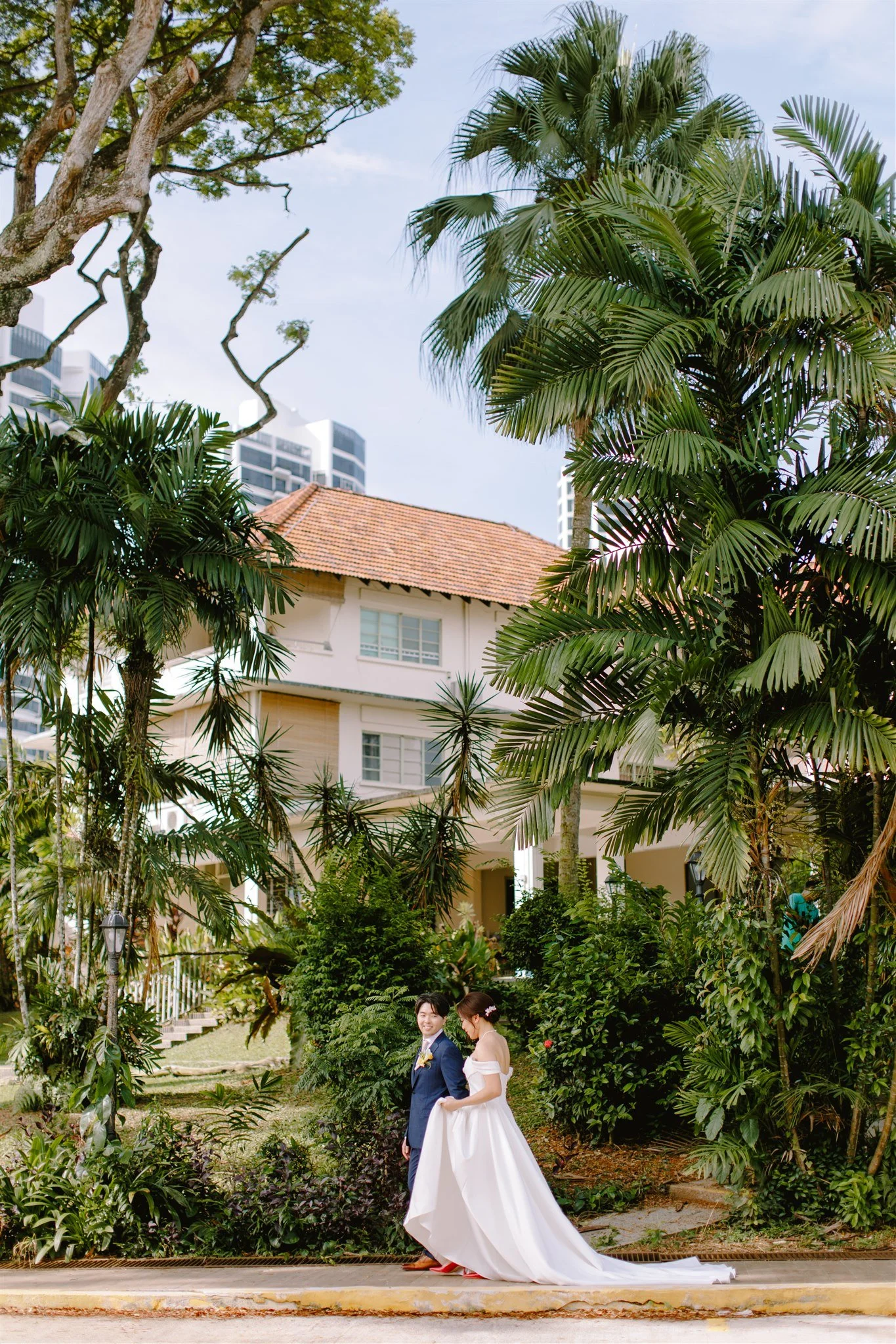 Bride and groom walking hand in hand through the lush gardens of Caroline’s Mansion, surrounded by greenery on their Singapore wedding day.