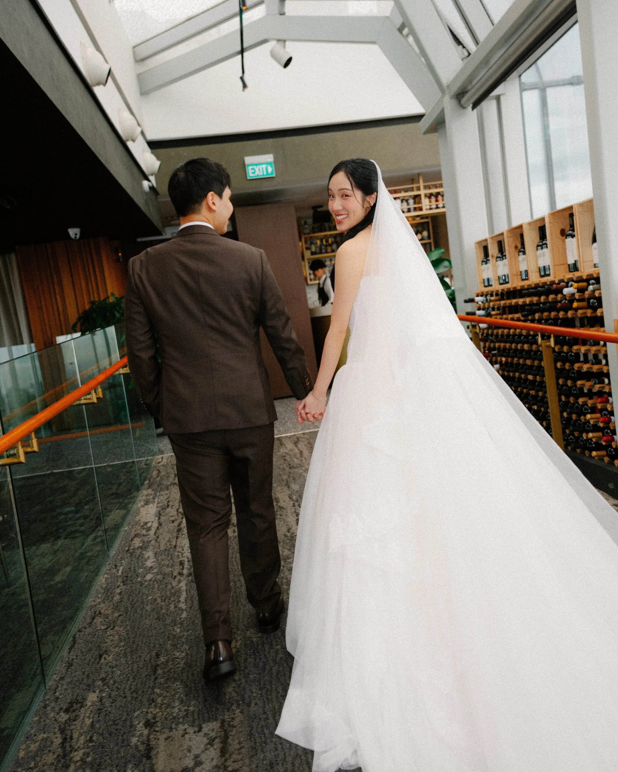 ride in flowing veil walking hand in hand with groom in brown suit at 1-Atico Singapore wedding venue.
