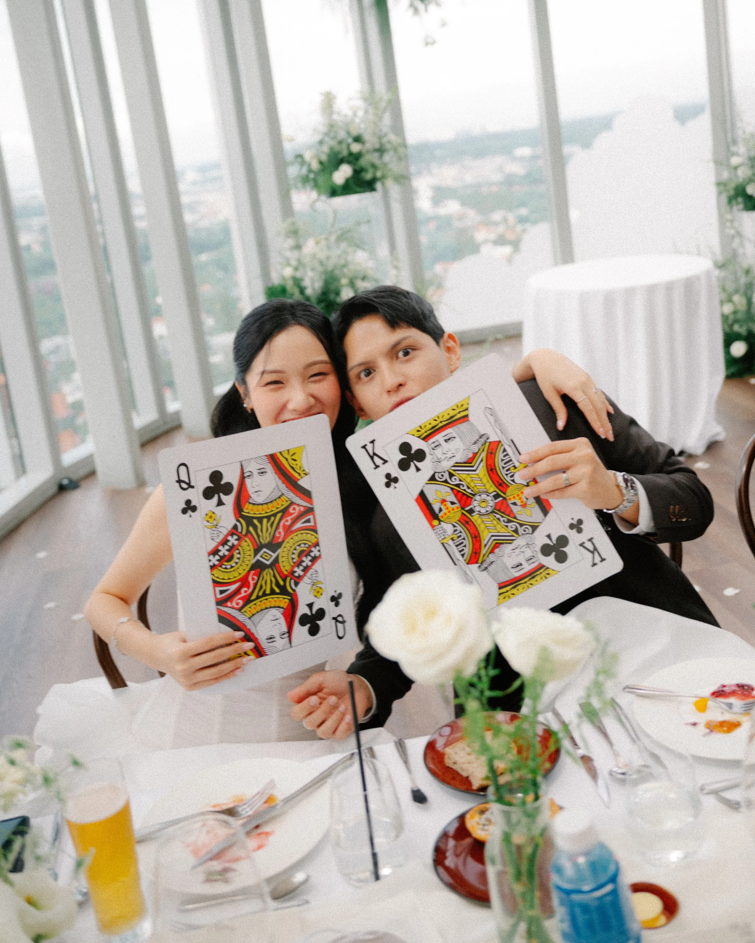 Bride and groom holding oversized playing cards during playful wedding reception moment at 1-Atico.