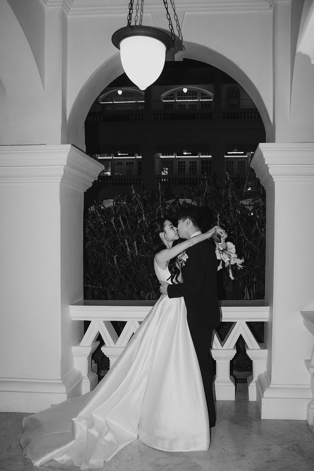 Bride and groom embracing beneath the arches of Raffles Hotel Singapore during evening wedding portraits