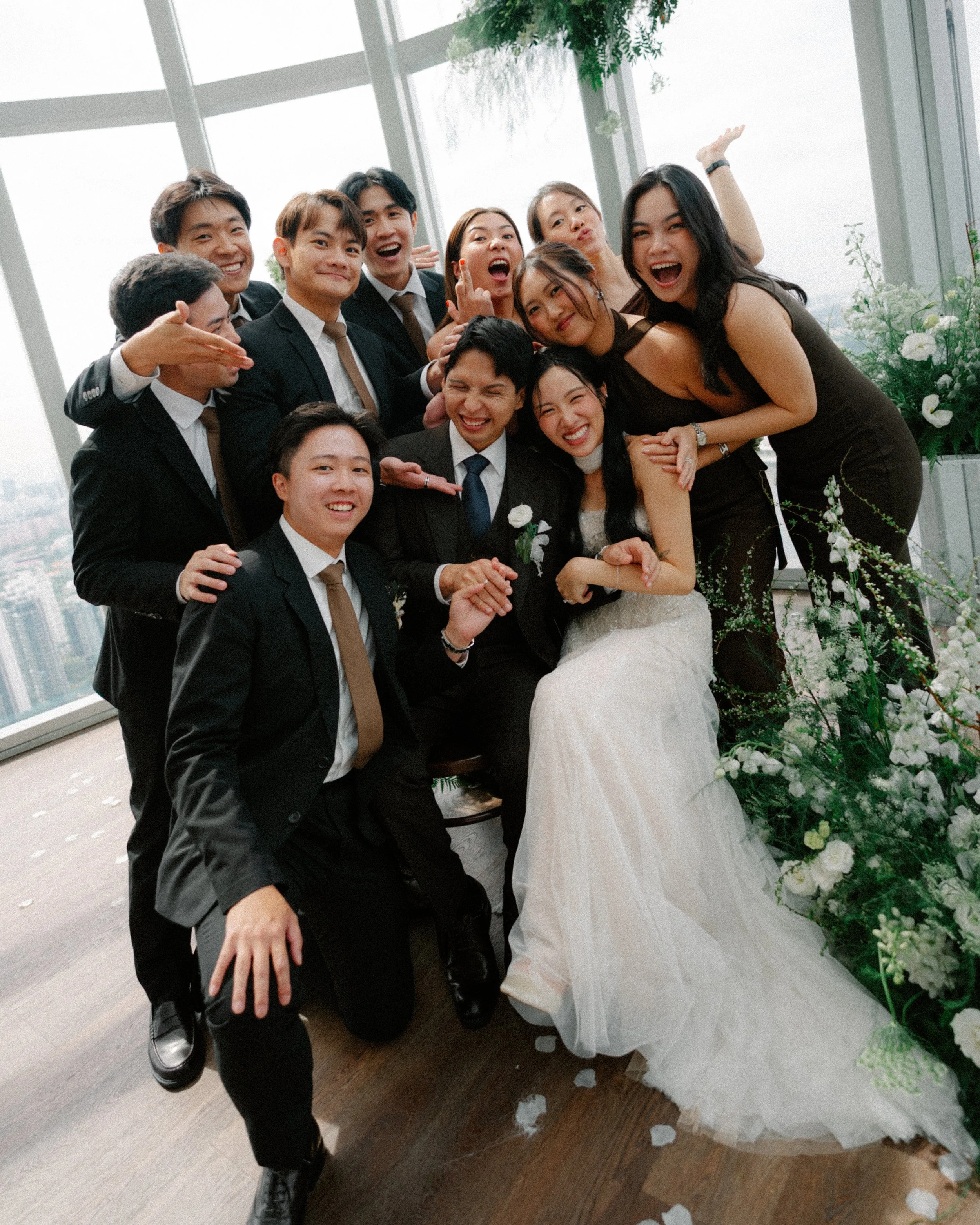 Wedding party in coordinated dark brown dresses and suits at 1-Atico Singapore wedding with white wildflower florals.