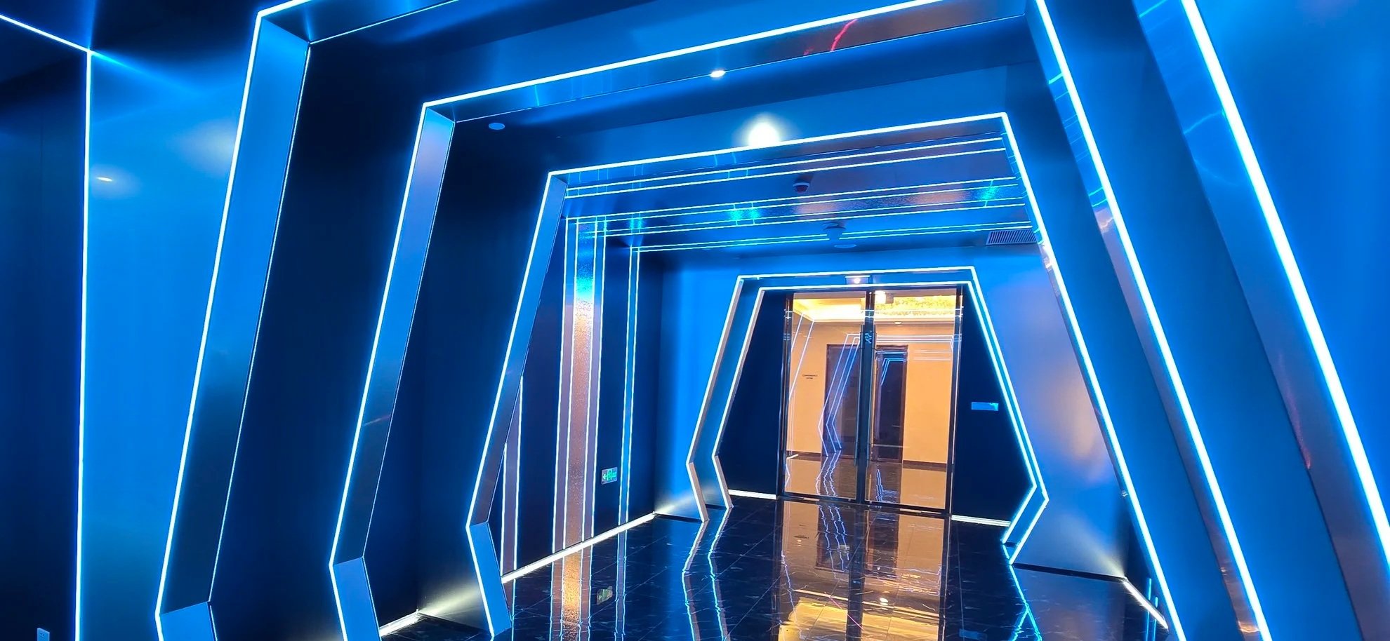 Futuristic corridor with blue neon lights and geometric shapes, leading to a glass door.