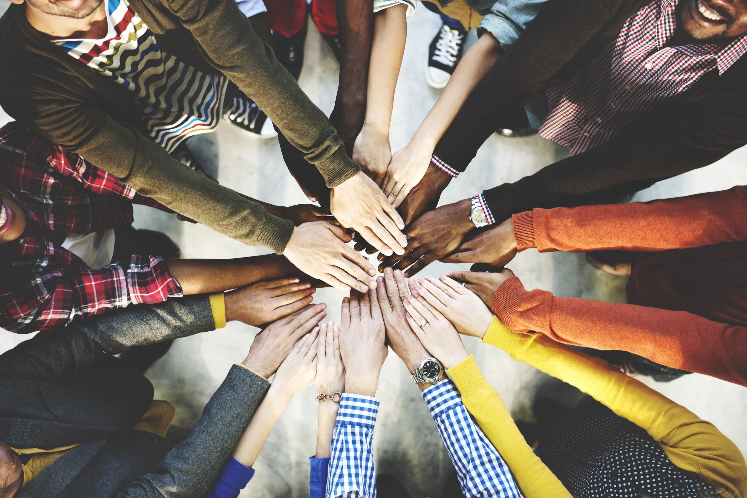 Multiple diverse people placing their hands together in a circle, symbolizing unity and teamwork.