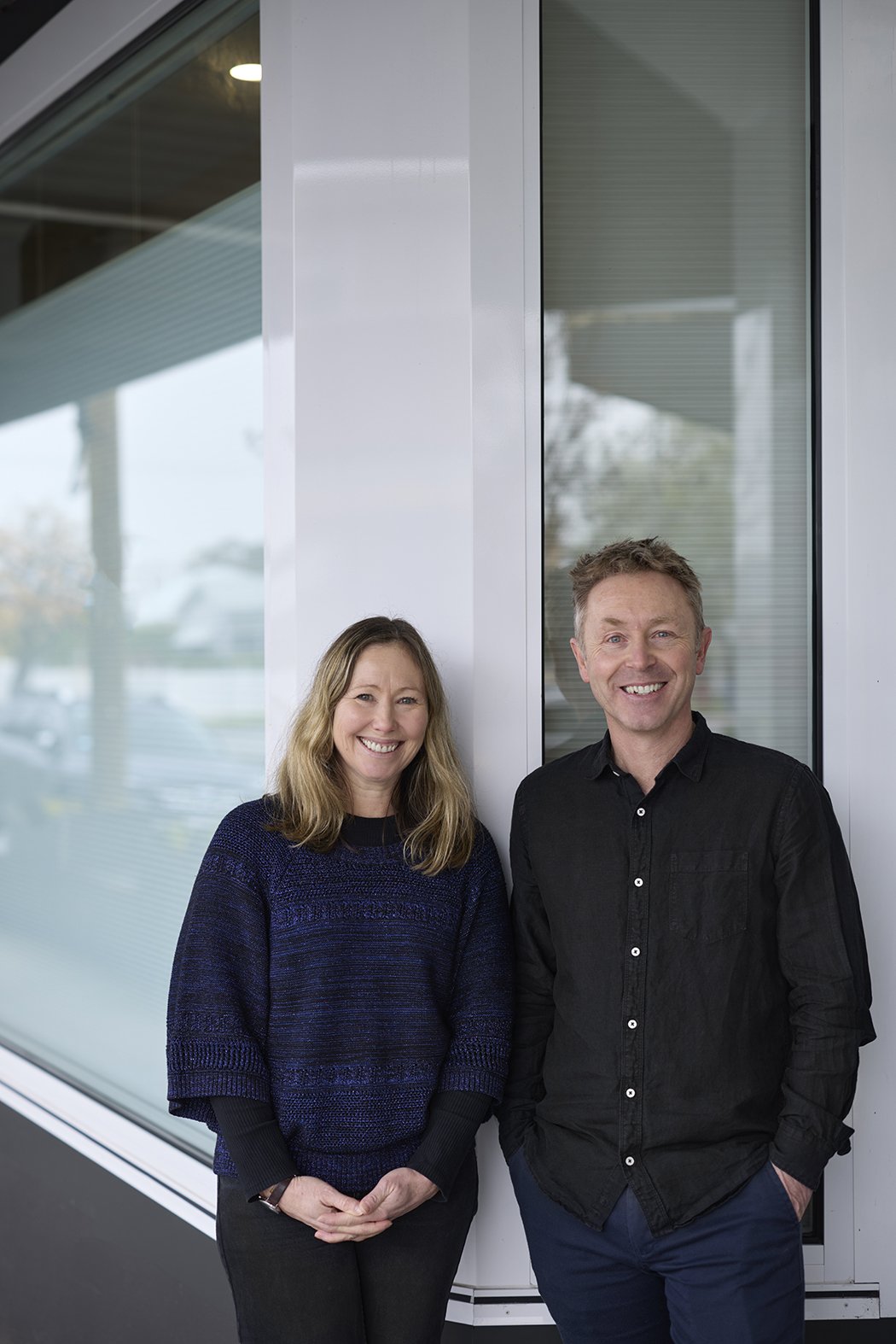 Meet Kristen Fawcett and Tim Jezard, the Directors of NCPS. They are smiling and standing side by side indoors near a glass window.
