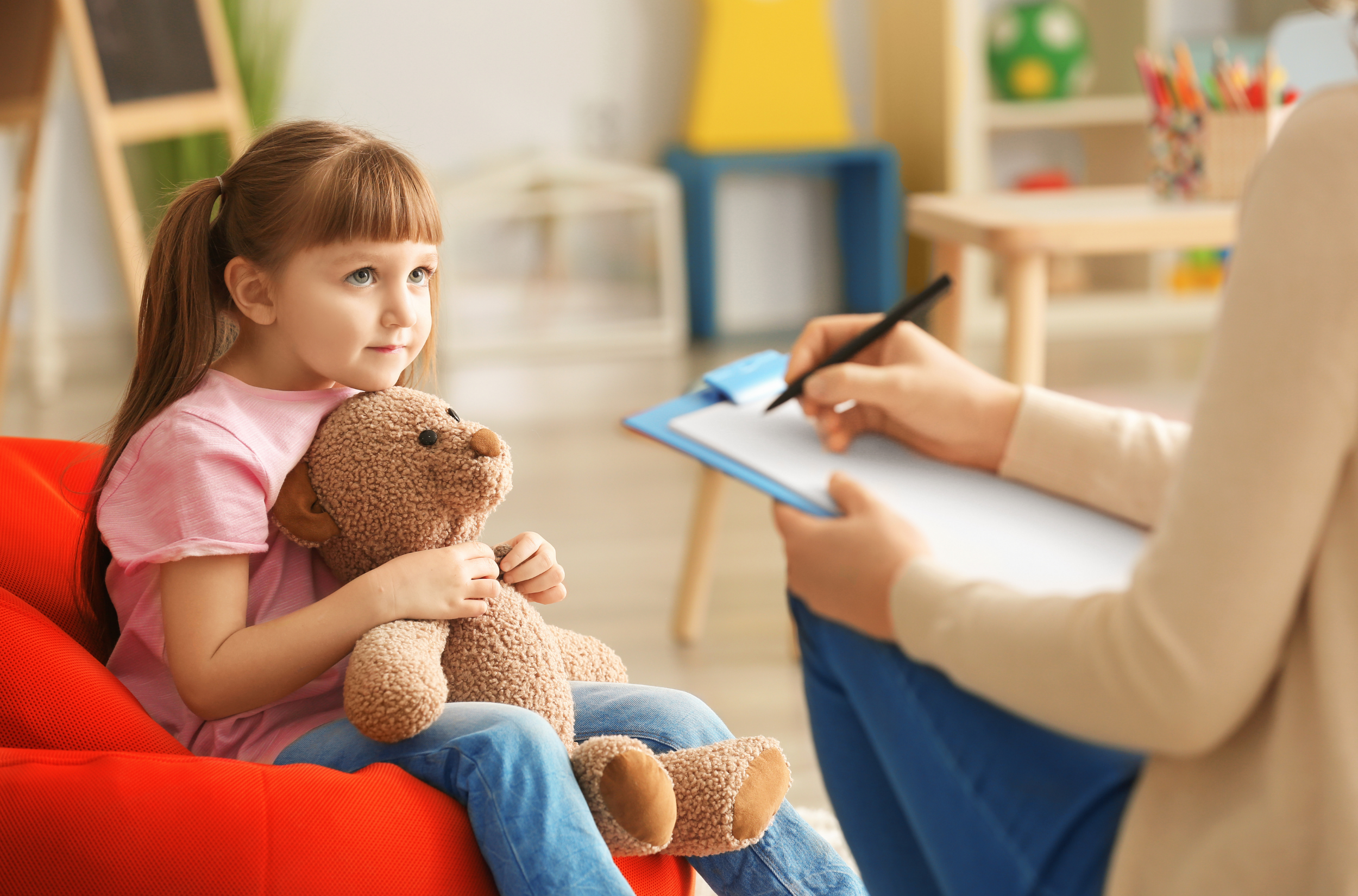 Young girl holding a teddy bear talks with a psychologist during a child therapy session