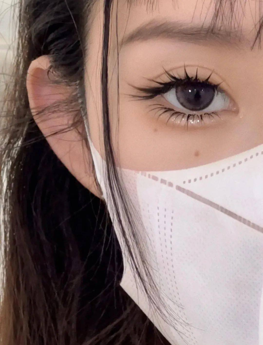 Close-up of a woman's eye wearing a white face mask.