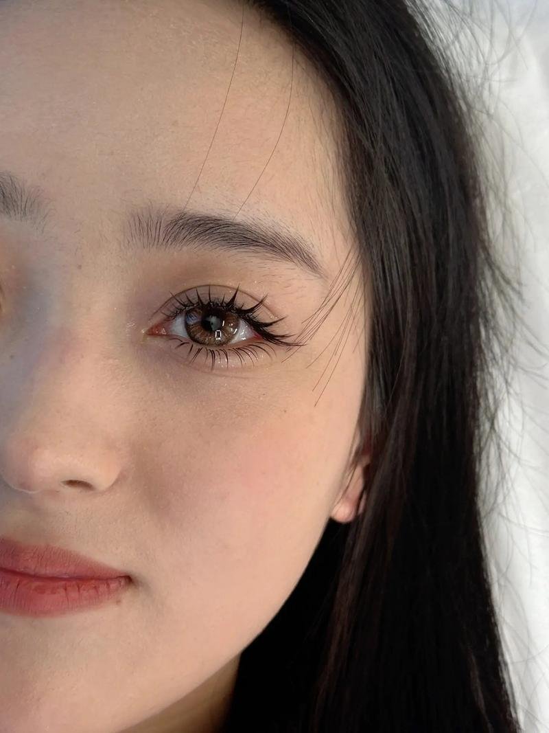 Close-up of a woman's face with long eyelashes and black hair, looking to the side.