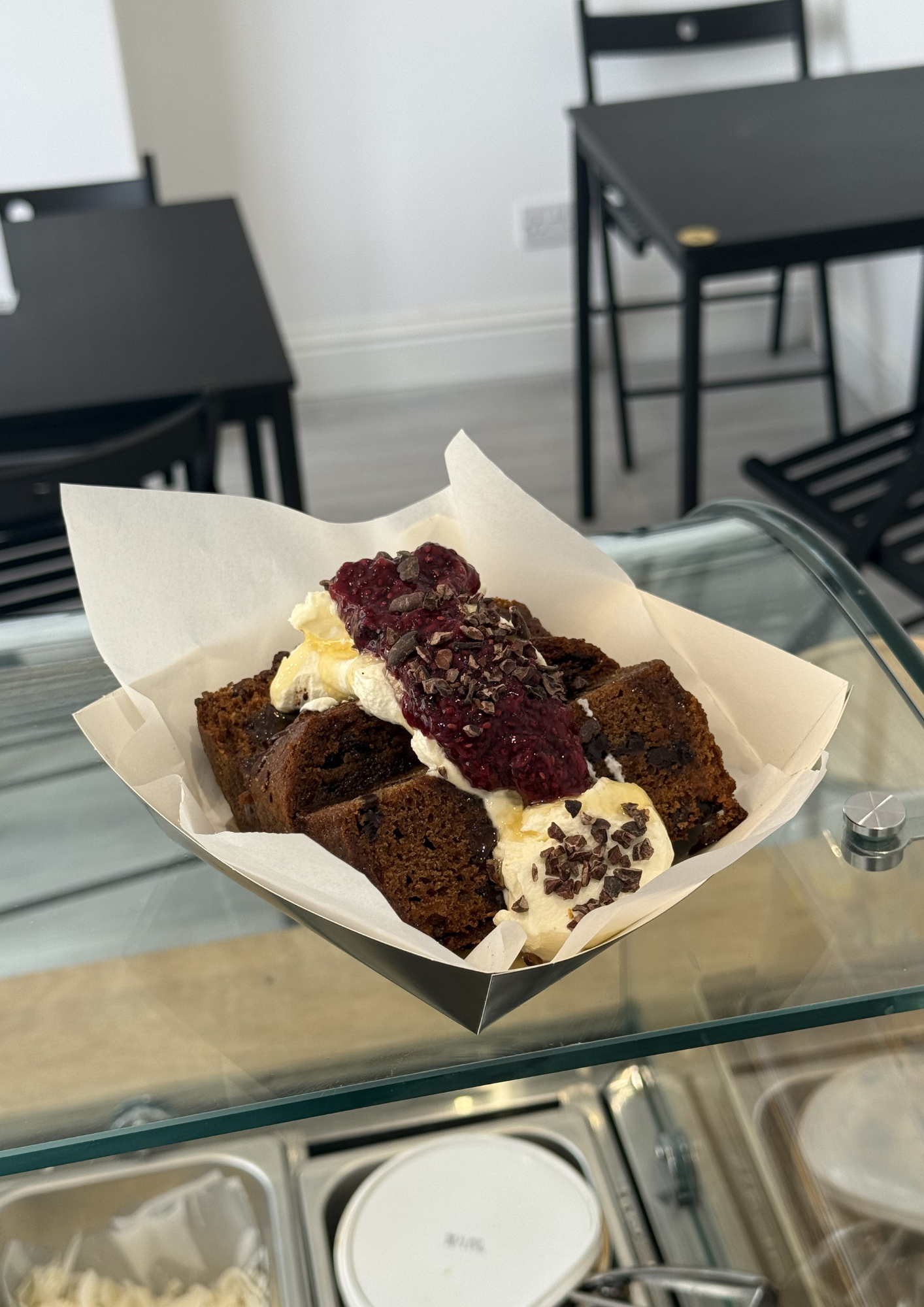 A slice of chocolate cake topped with whipped cream, raspberry sauce, and chocolate shavings on a piece of white parchment paper.