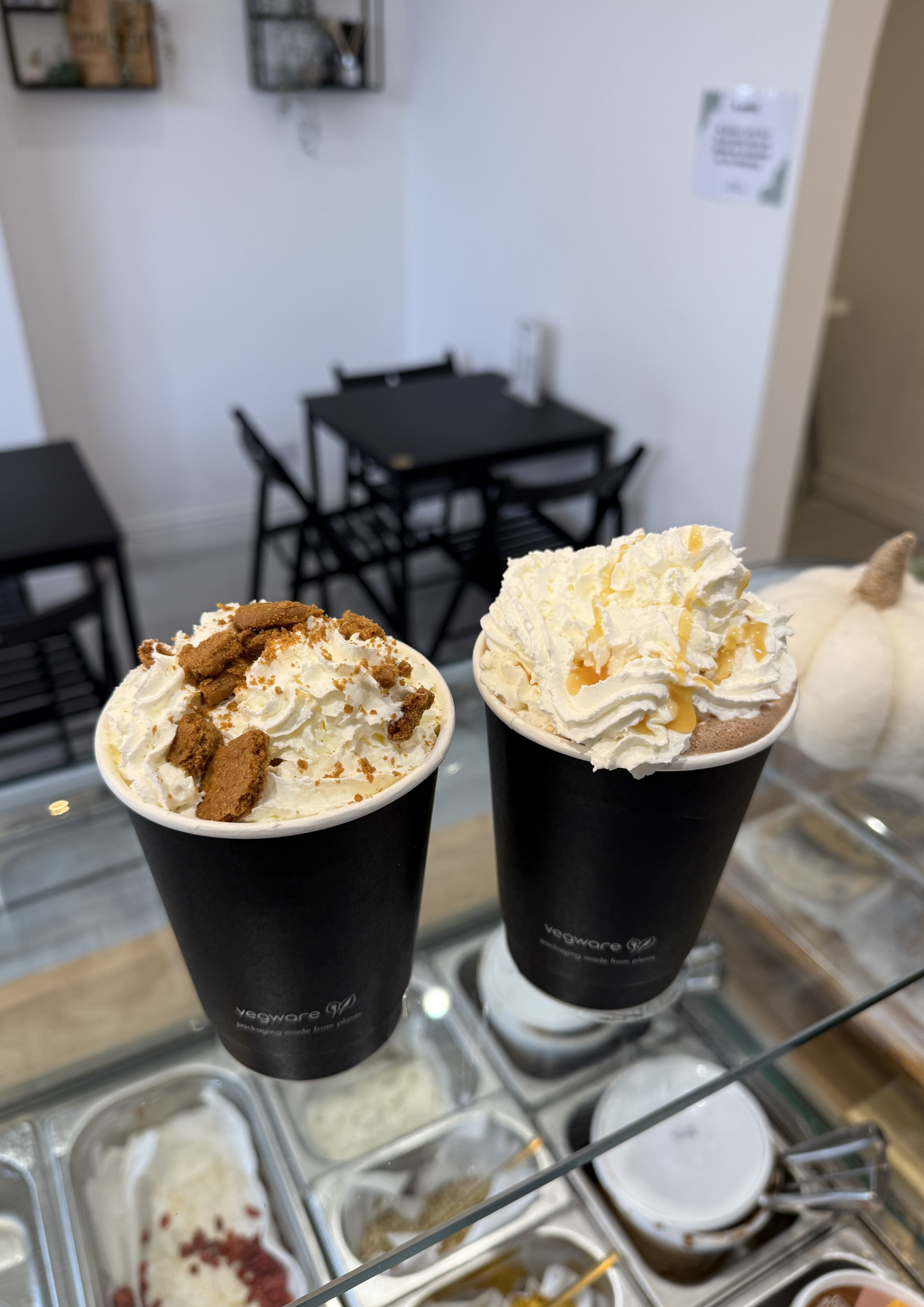 Three cups of whipped cream topped with cookie crumbs and caramel sauce, with a background of ice cream tubs.